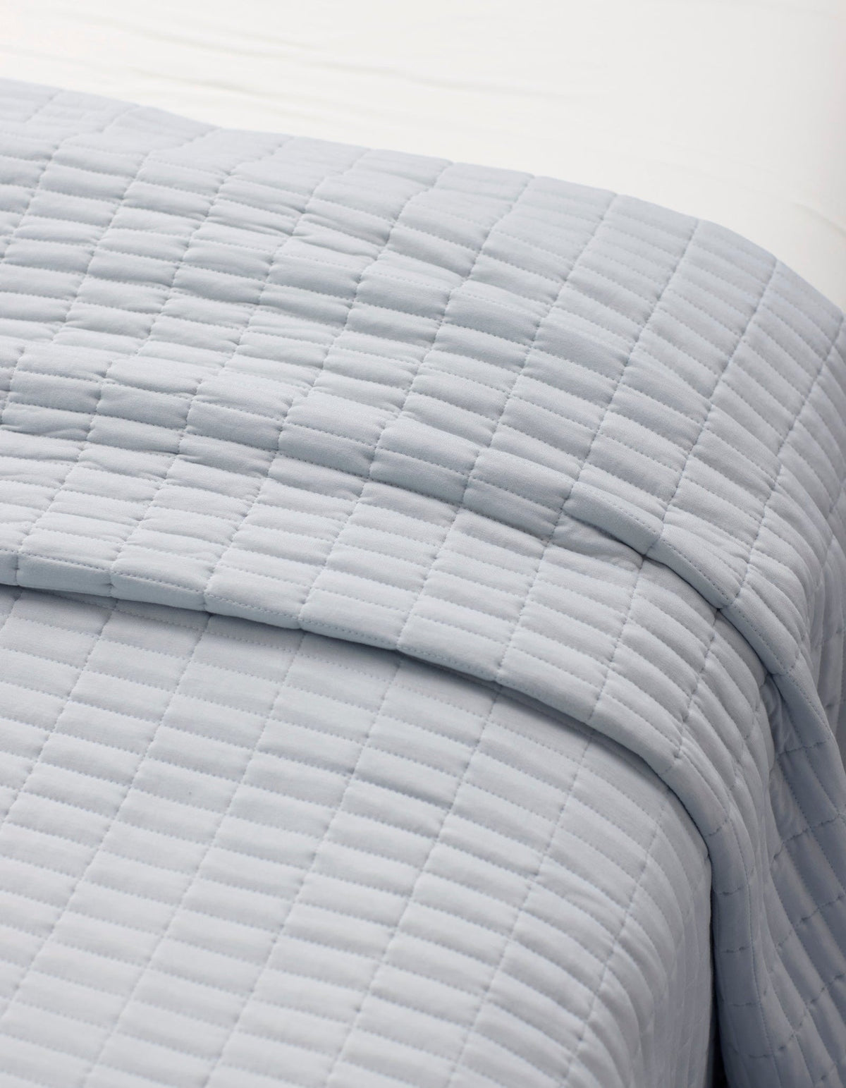 A close-up of a neatly made bed with the Cozy Earth Bamboo Jersey Quilt Bundle, featuring a light gray, square-patterned quilt layered over white sheets.|Color:Shore