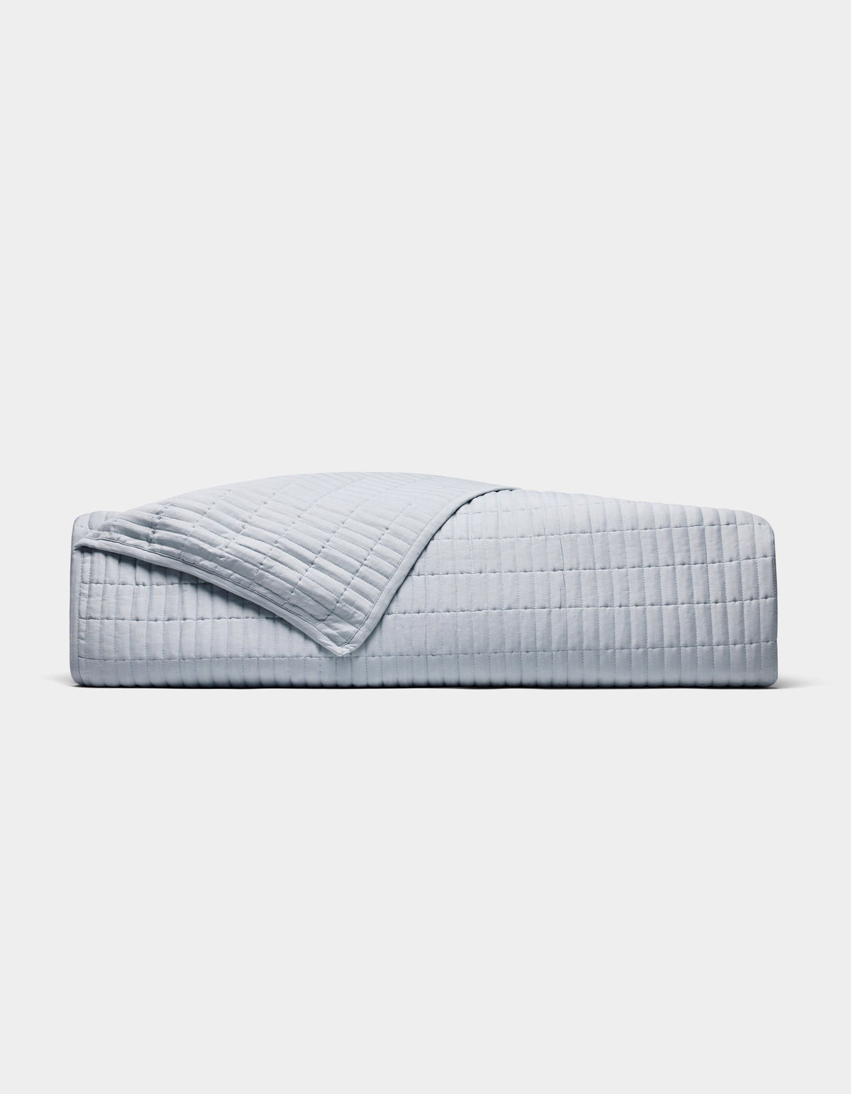 A neatly made bed displays the Cozy Earth Bamboo Jersey Quilt in light grey with a matching pillow, one quilt corner folded back, all set against a plain white background.|Color:Shore