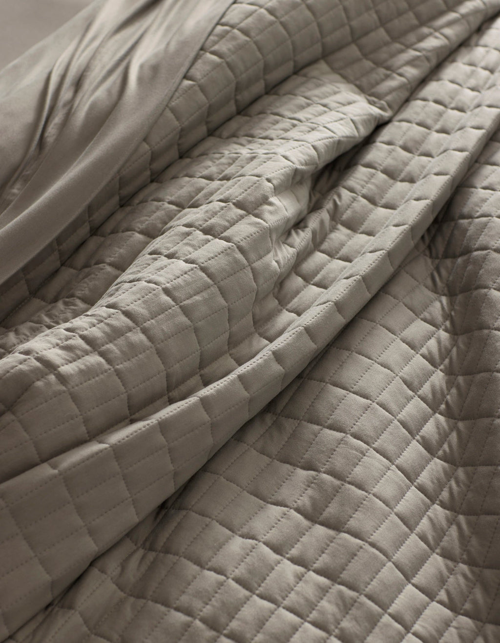 Close-up of the Cozy Earth Bamboo Jersey Quilt in light gray, featuring a quilted grid pattern with visible folds and soft texture for a cozy, inviting look.|Color:Stone
