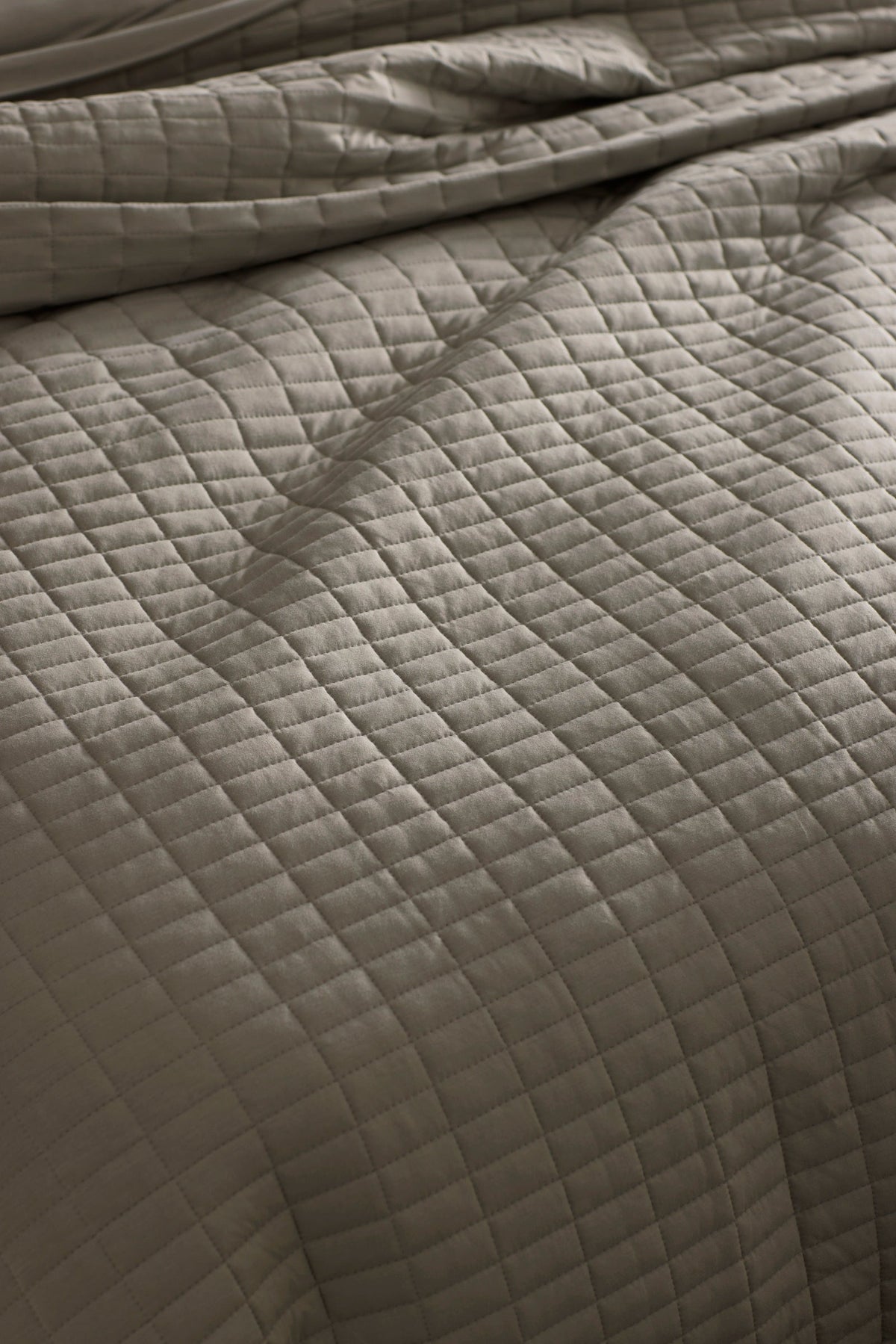 Close-up of a neatly made bed with the Cozy Earth Bamboo Jersey Quilt Bundle, featuring a soft, slightly wrinkled quilt in a light neutral tone with a grid of stitched squares.