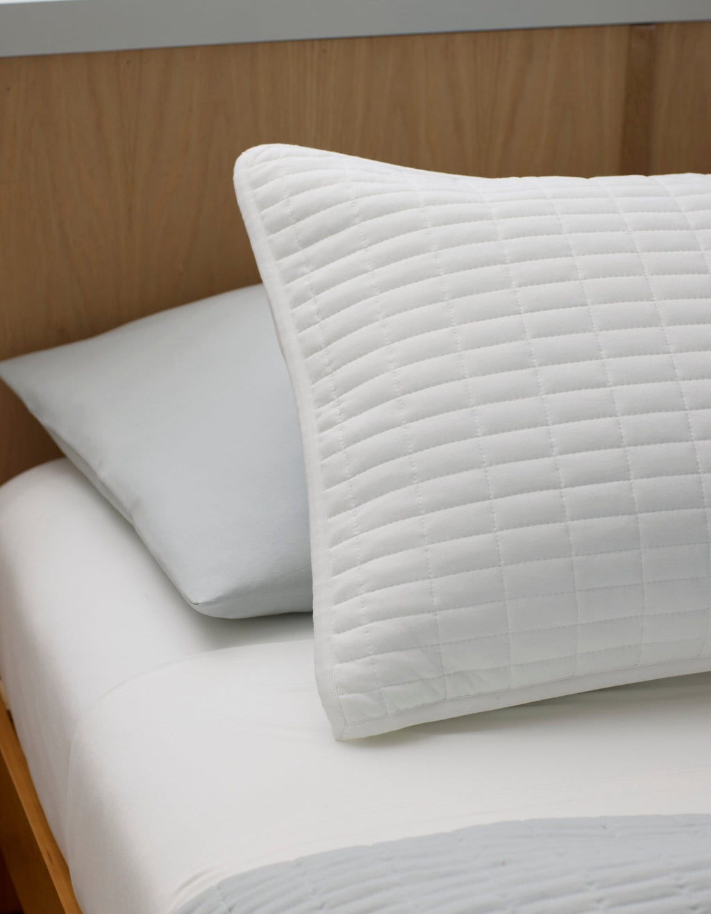 The Bamboo Jersey Quilt Bundle by Cozy Earth features a front pillow with a white, quilted grid cover and a back pillow in plain light gray, styled on a neatly made bed with a simple, minimalist aesthetic.|Color:White