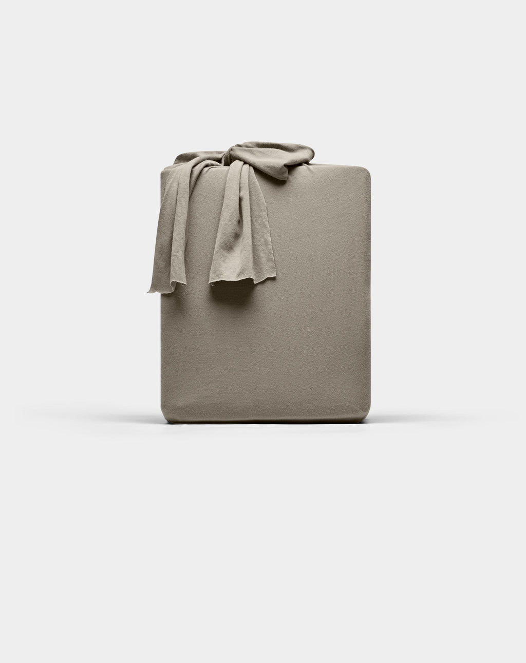 A taupe Cozy Earth Bamboo Jersey fitted sheet is neatly folded with one corner draped over the top, displayed against a plain white background.|Color:Stone