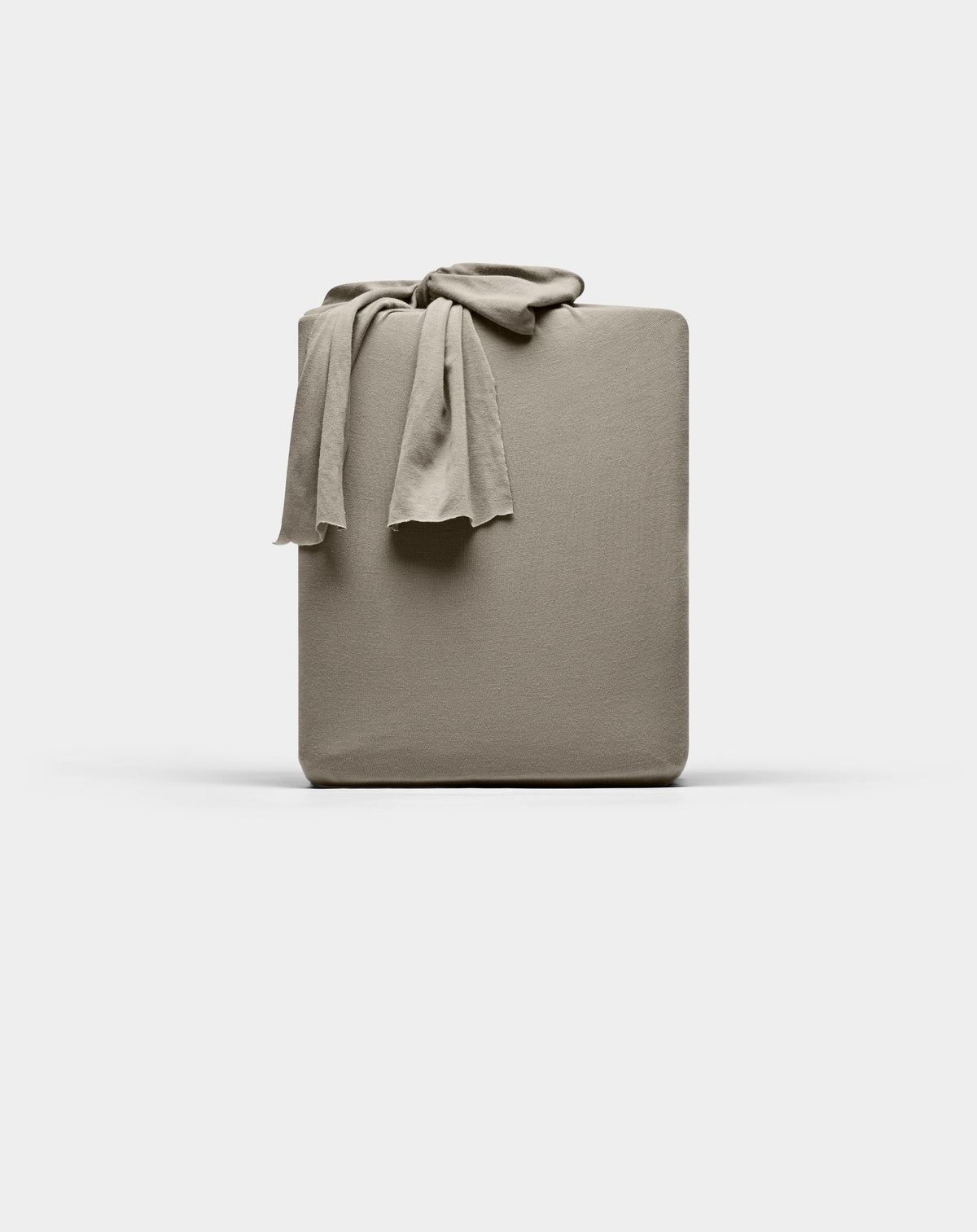 A taupe Cozy Earth Bamboo Jersey fitted sheet is neatly folded with one corner draped over the top, displayed against a plain white background.|Color:Stone