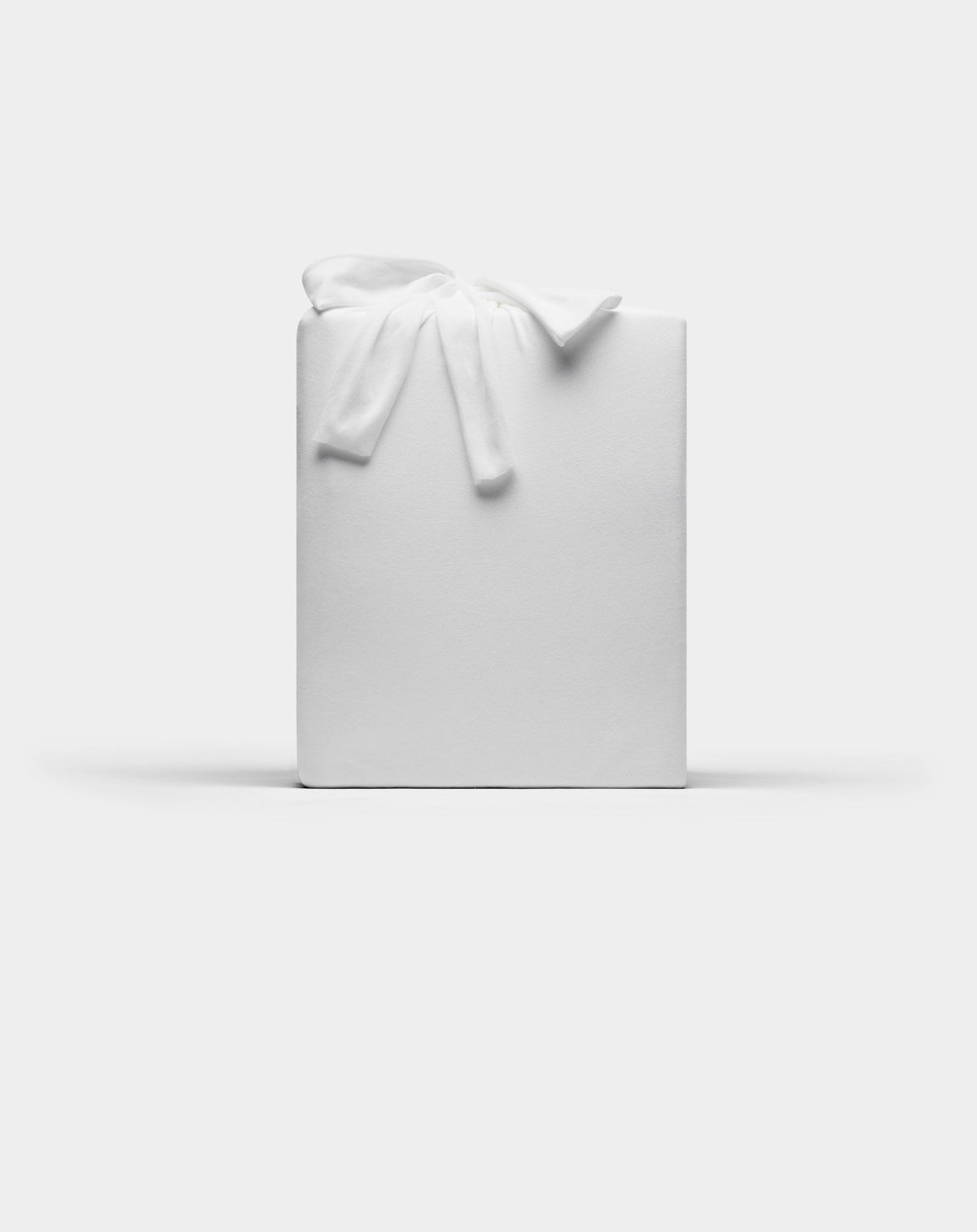A Bamboo Jersey Sheet Set by Cozy Earth, wrapped in plain white paper with a white fabric bow on top, set against a plain white background.|Color:White