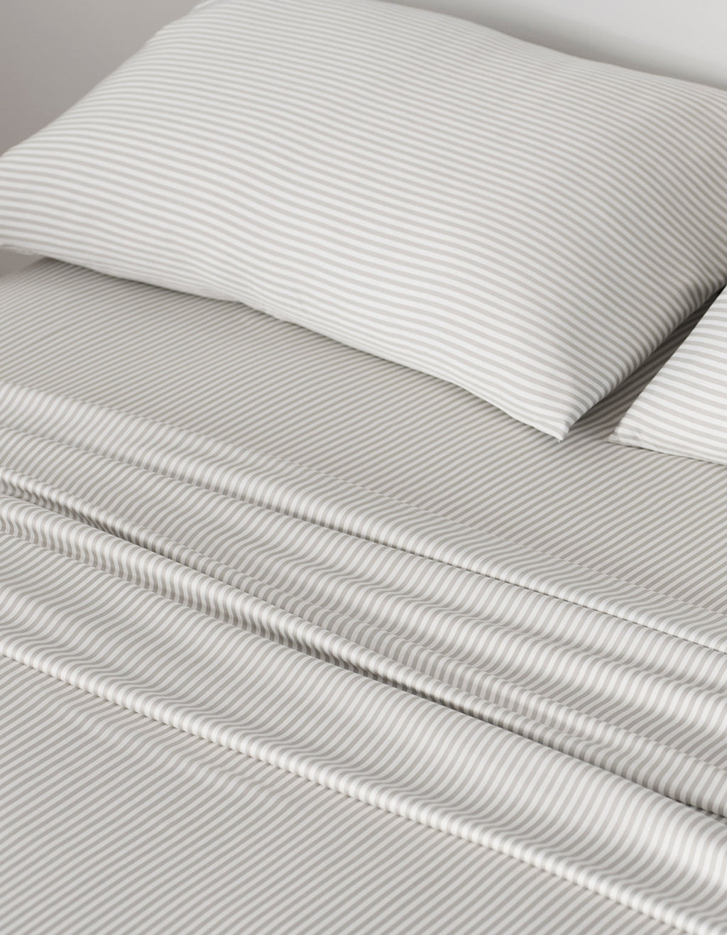 A neatly made bed showcases Cozy Earth Bamboo Pillowcases and sheets with thin, light gray and white horizontal stripes, giving the bedding a smooth, clean look that creates a calm and cozy atmosphere.|Color:Classic Stripe in Laurel