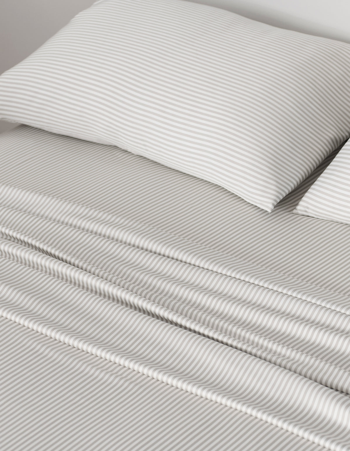 A neatly made bed showcases Cozy Earth Bamboo Pillowcases and sheets with thin, light gray and white horizontal stripes, giving the bedding a smooth, clean look that creates a calm and cozy atmosphere.|Color:Classic Stripe in Laurel