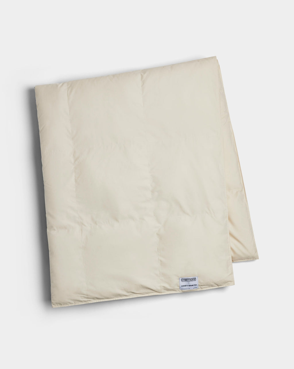 The Cozy Earth Down Alternative Throw is a folded, cream-colored quilt with a small rectangular label near the edge, displayed on a white background.|Color:Coconut
