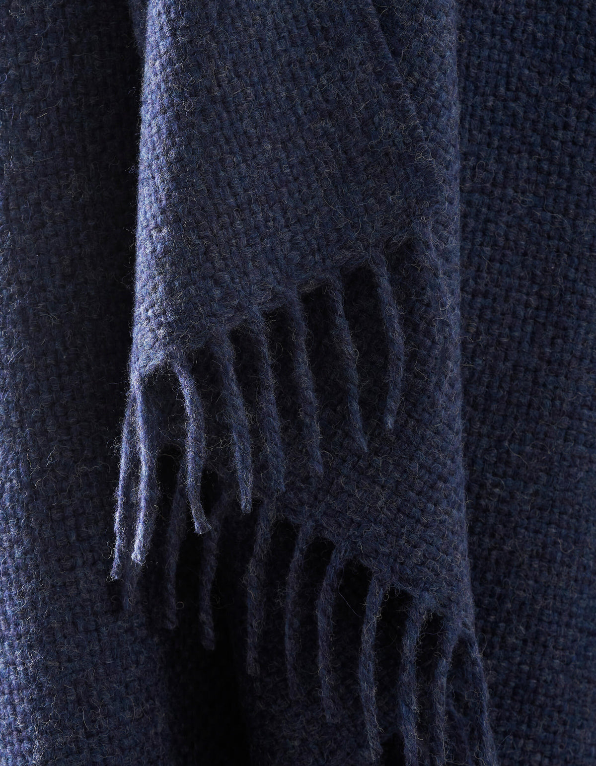 A close-up of the Lucia Throw by Cozy Earth shows its dark blue, textured woven fabric with fringed edges hanging down.|Color:Indigo