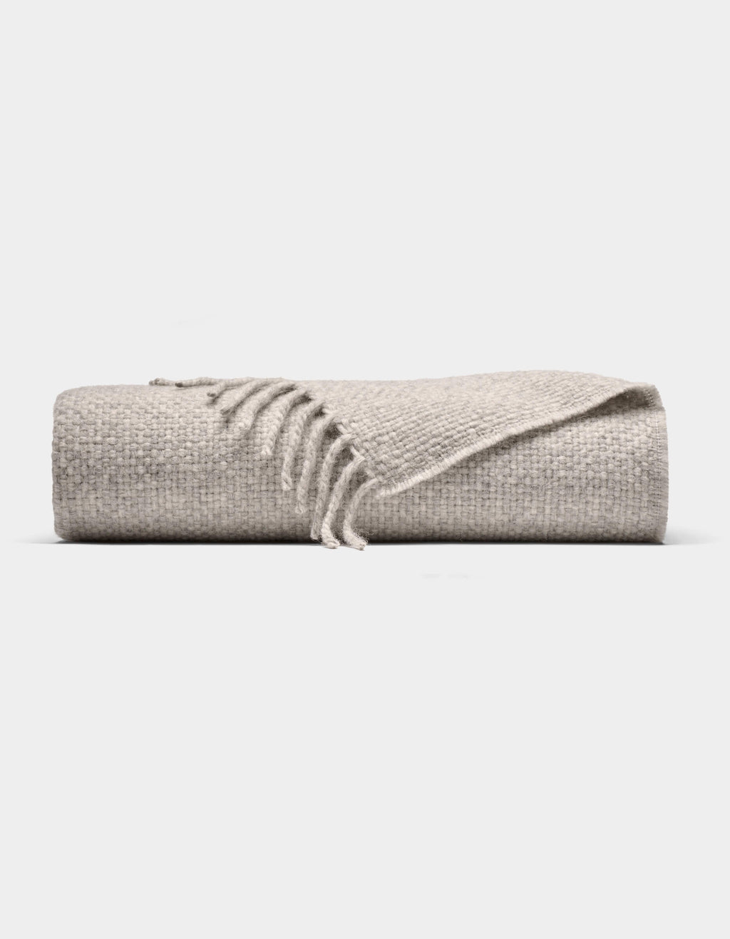 The Cozy Earth Lucia Throw is a folded light gray woven blanket with a textured surface and fringe on one end, shown against a plain white background.|Color:Soft Grey