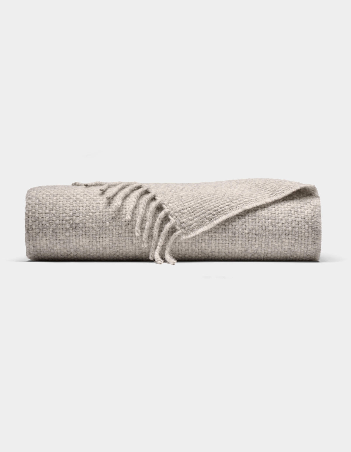 The Cozy Earth Lucia Throw is a folded light gray woven blanket with a textured surface and fringe on one end, shown against a plain white background.|Color:Soft Grey