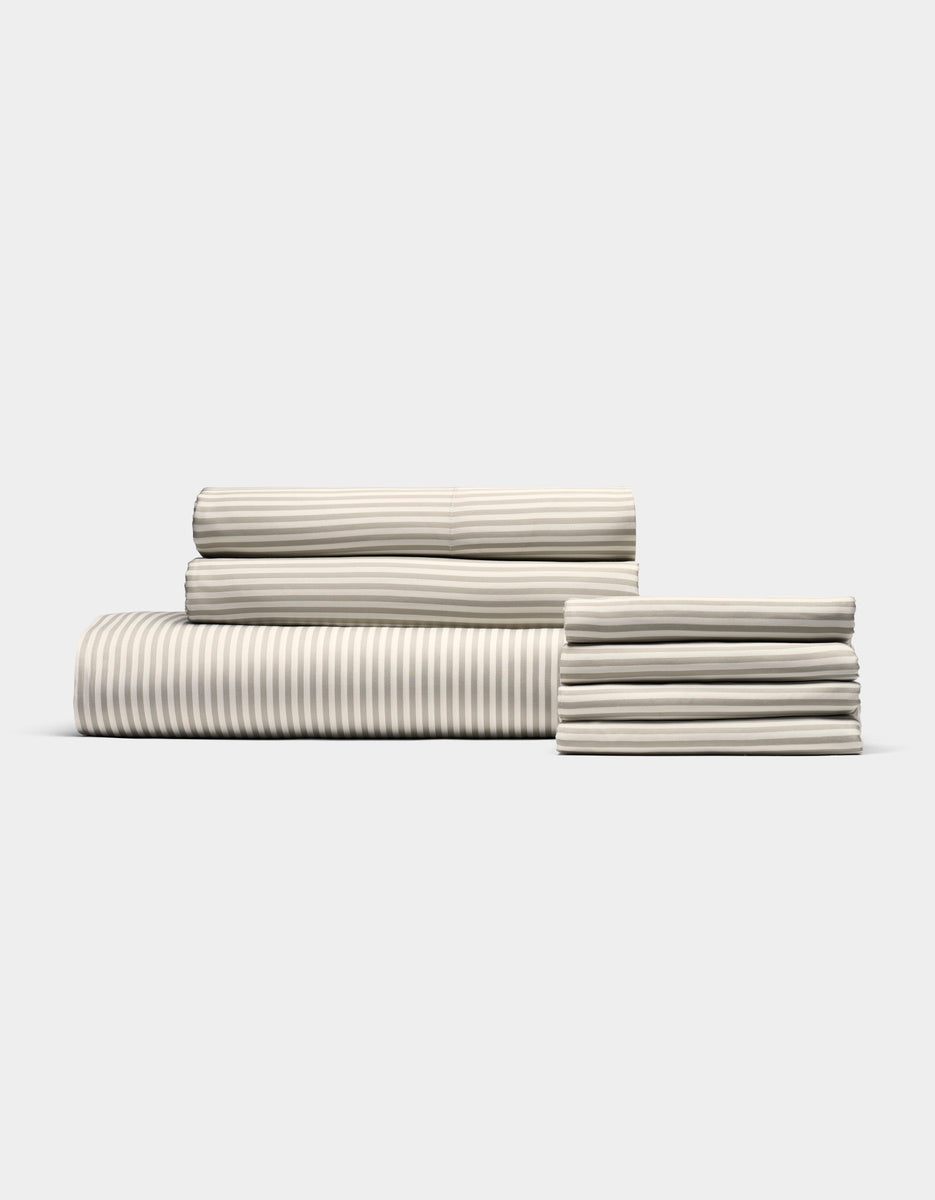 The Cozy Earth Bamboo Bedding Core Bundle features neatly folded cream-colored sheets with subtle light gray stripes, arranged on a plain white background.|Color:Classic Stripe in Laurel