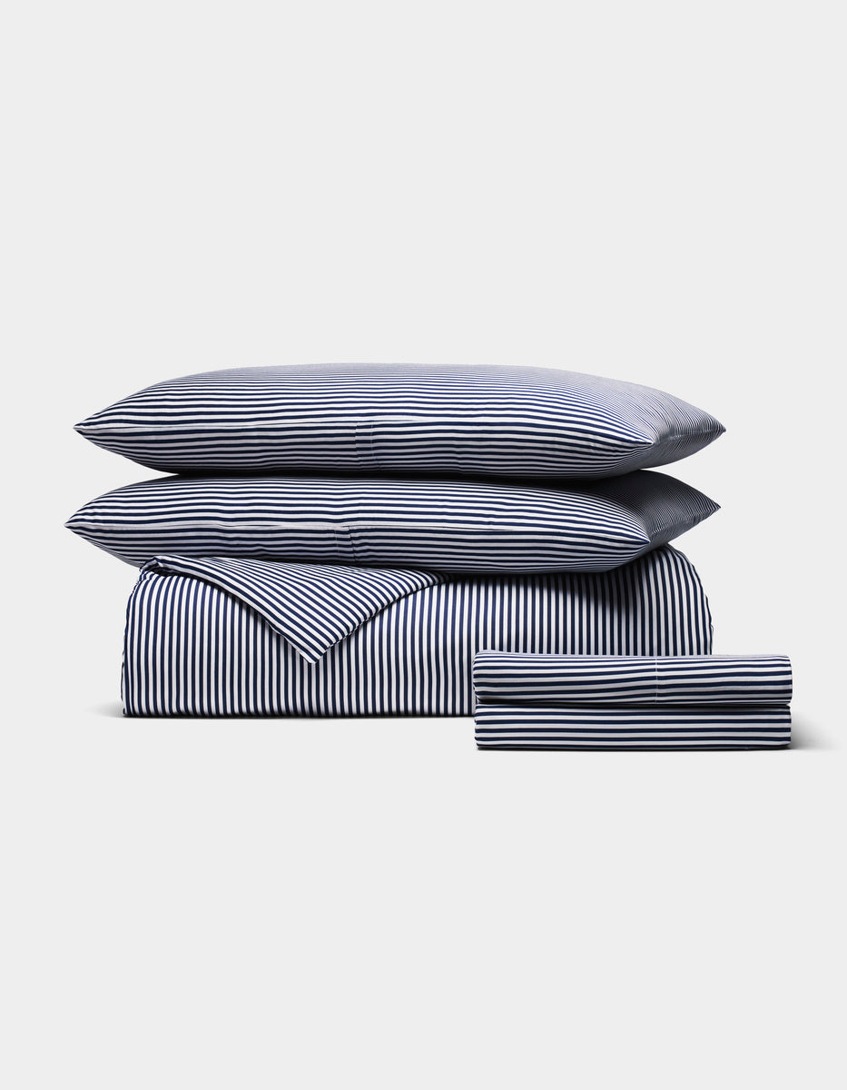 The Cozy Earth Bamboo Bedding Deluxe Bundle, featuring two pillows, a duvet, and sheets with navy and white vertical stripes, is neatly folded and displayed against a plain light background.|Color:Classic Stripe in Pacific
