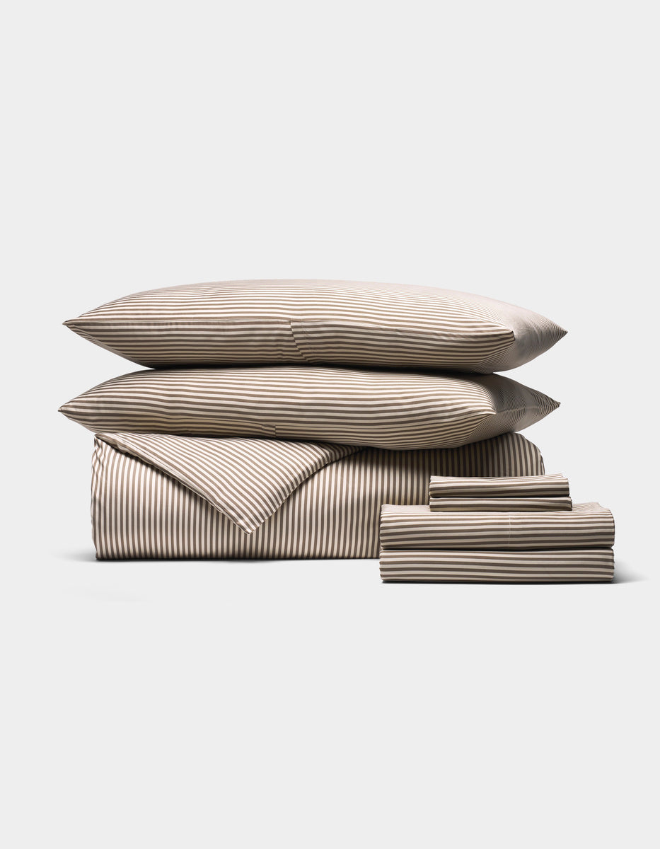 The Cozy Earth Bamboo Bedding Ultimate Bundle features two pillows, a comforter, and sheets in beige and white horizontal stripes, all neatly folded and arranged on a white background.|Color:Classic Stripe in Ebony
