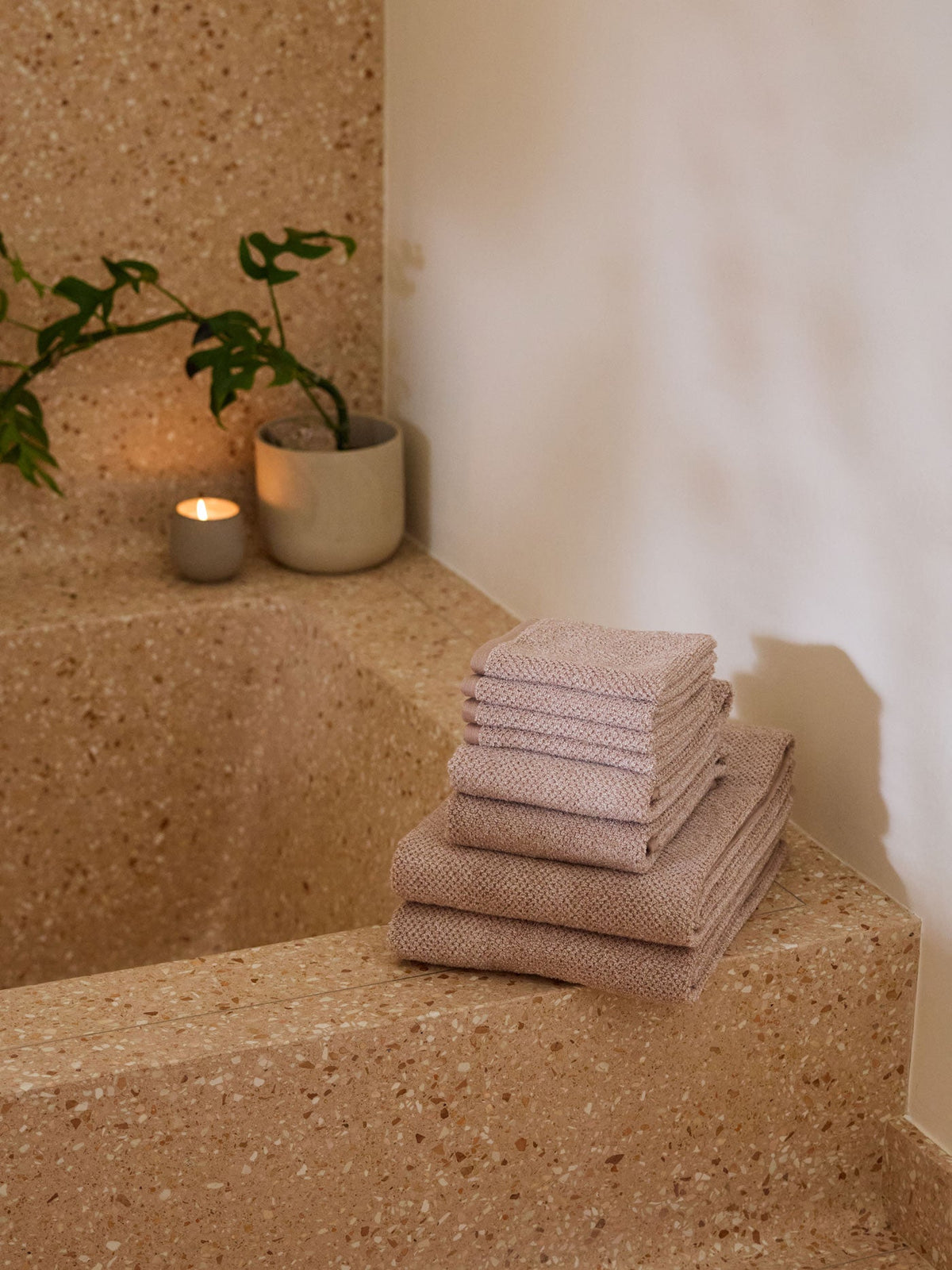A stack of Cozy Earth bath towels sit on the edge of a stone bathtub. |Color:Heathered Clay