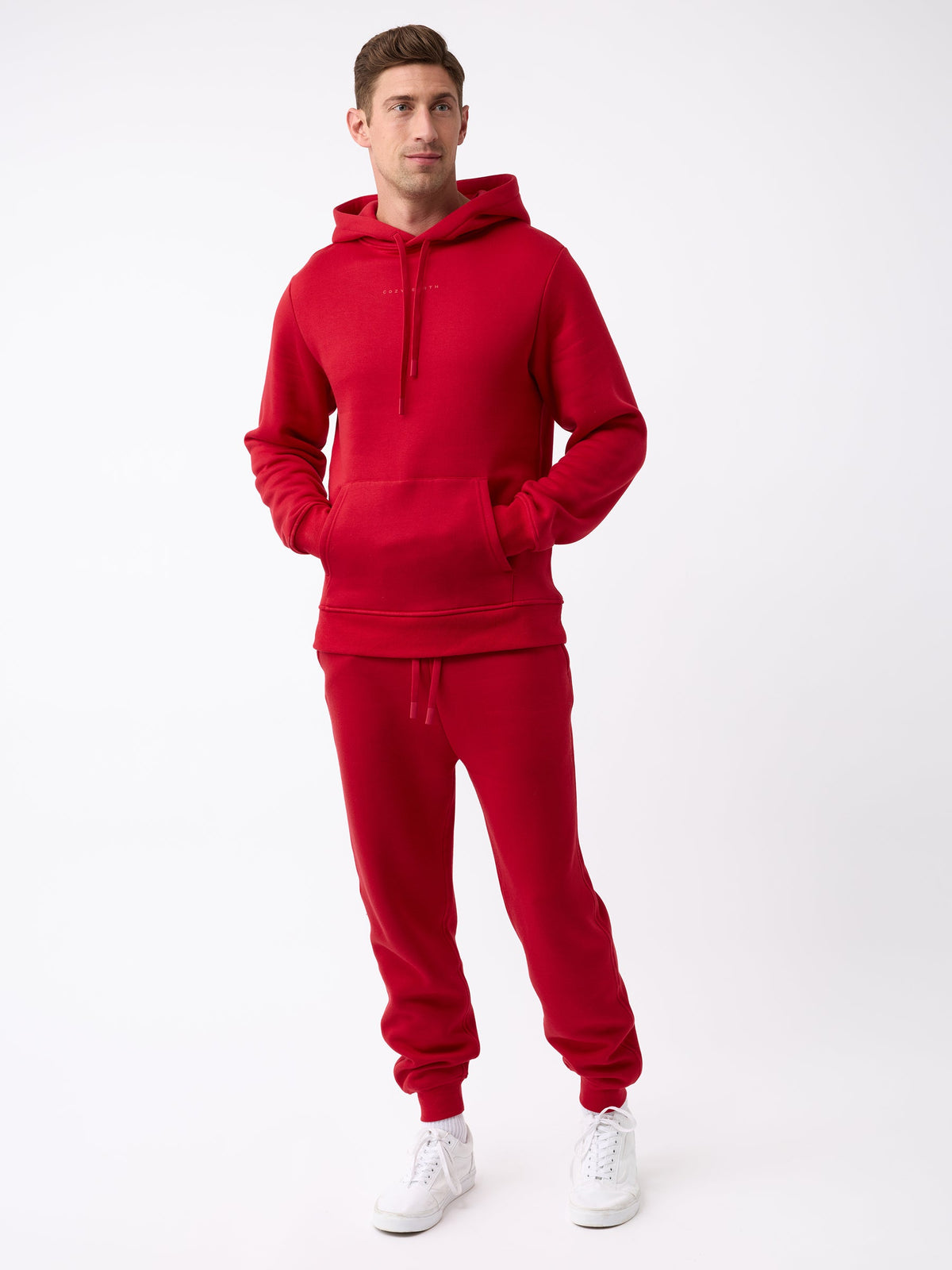 A person wearing a vibrant red Men's CityScape Jogger from Cozy Earth stands against a plain white background. They have one hand in their pocket and are looking slightly to the side while also wearing white sneakers. |Color:Crimson