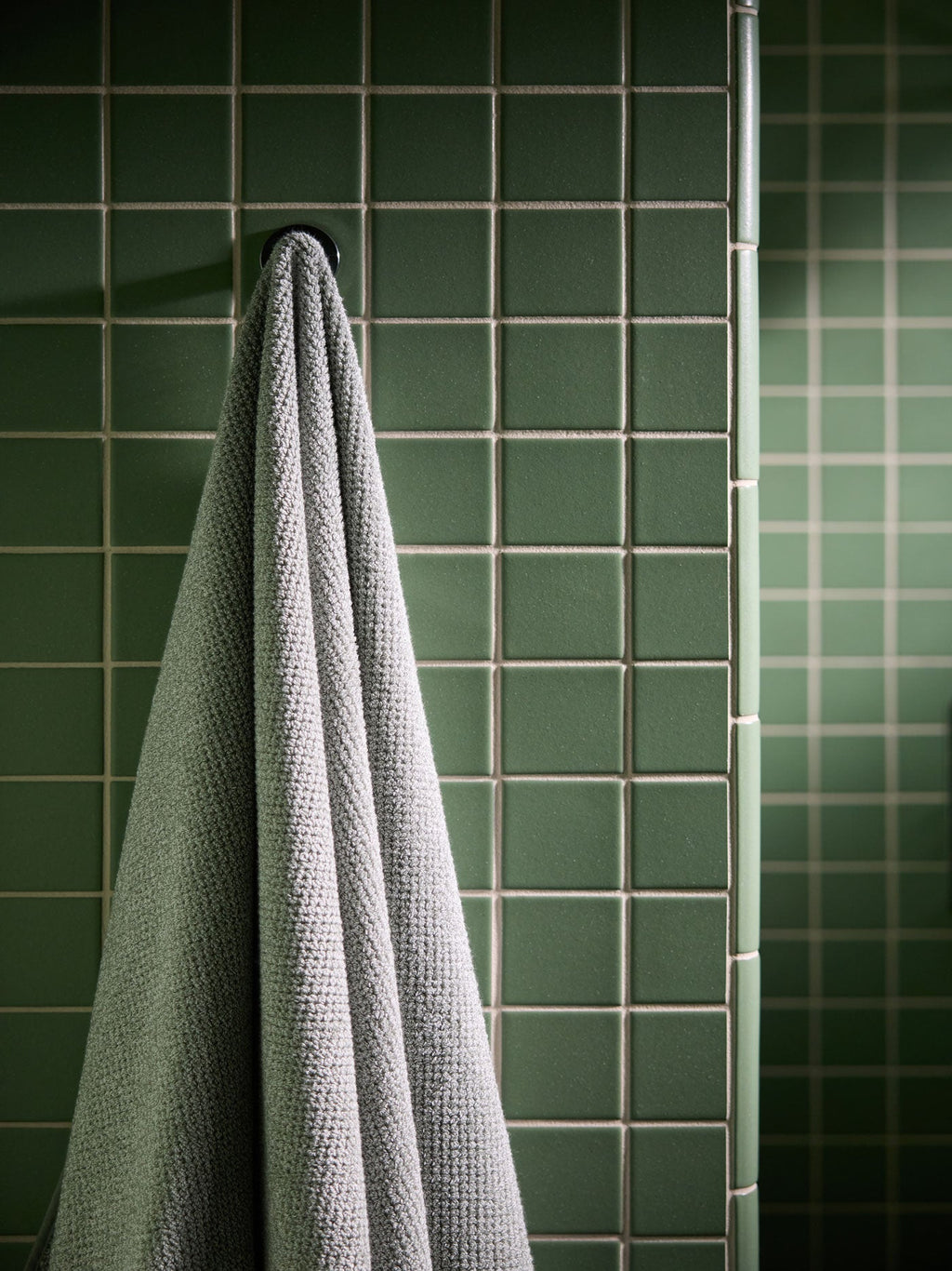 A Nantucket Bath Towel in Heathered Sage is shown hanging in a green tiled bathroom. |Color:Heathered Sage