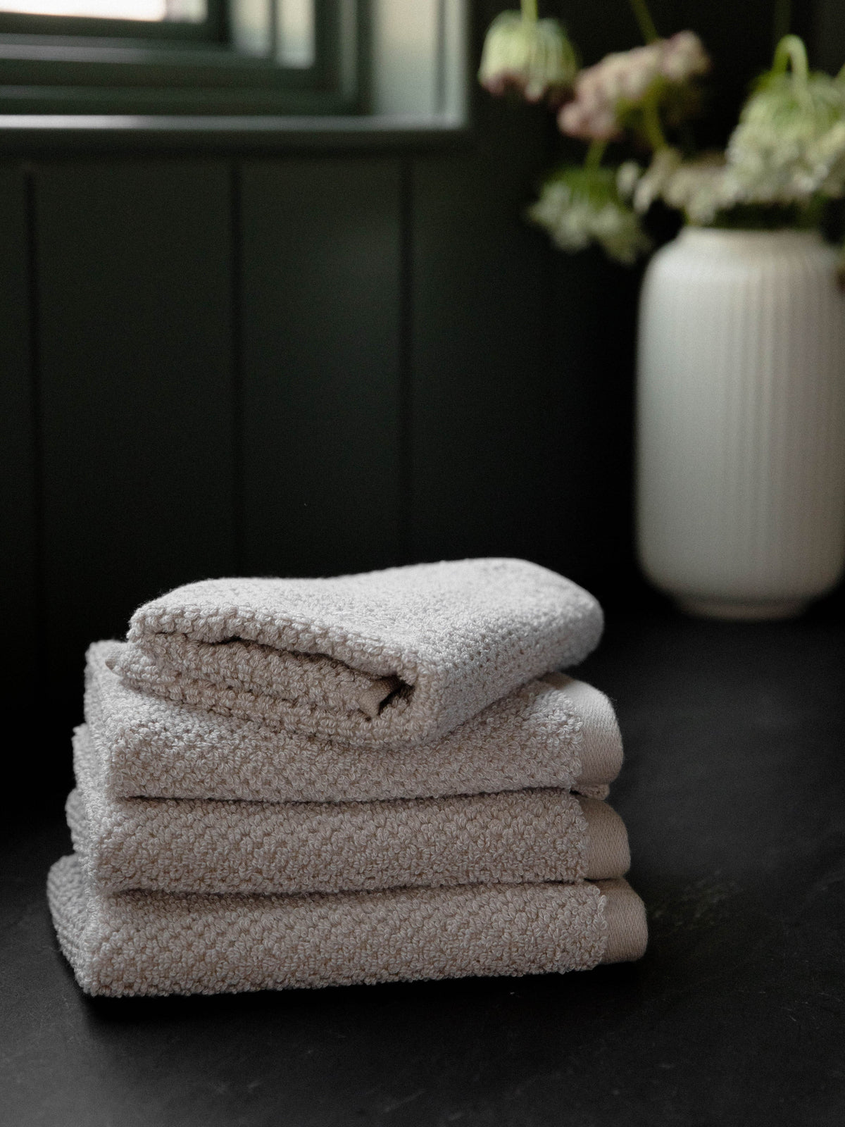 Nantucket Wash Cloths in the color Heathered Sand. Photo of Nantucket Wash Cloths taken with the Wash Cloths resting on a countertop in a bathroom. |Color:Heathered Sand