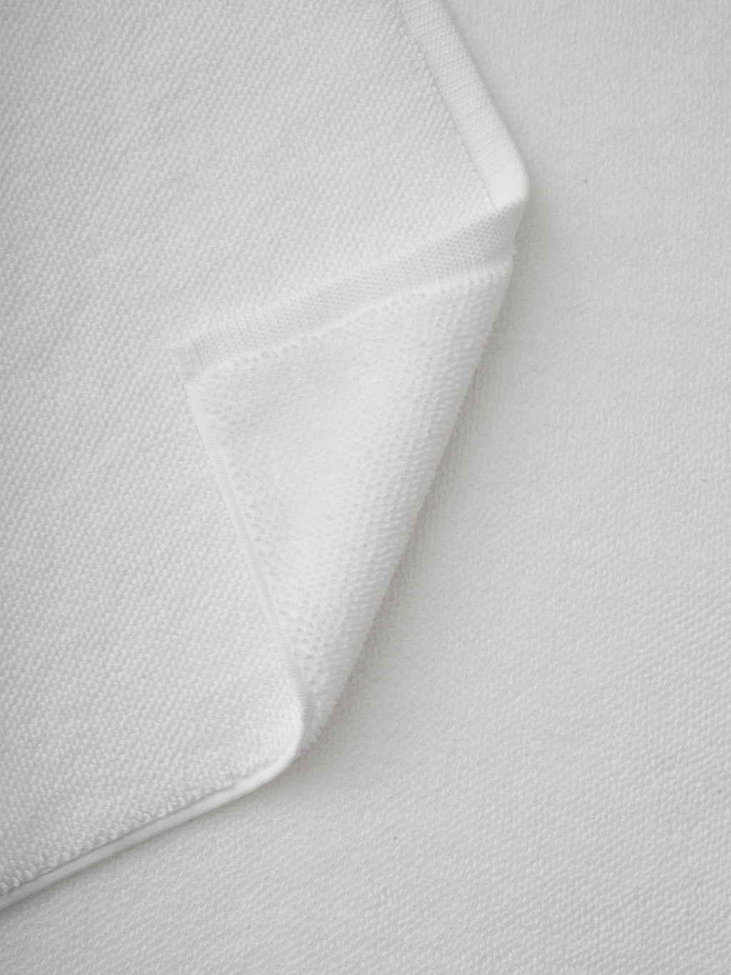 A close-up of the Cozy Earth Loop Terry Bath Mat with a folded corner highlights its soft, textured surface and neatly stitched edges, set against a background of the same material.|Color:White