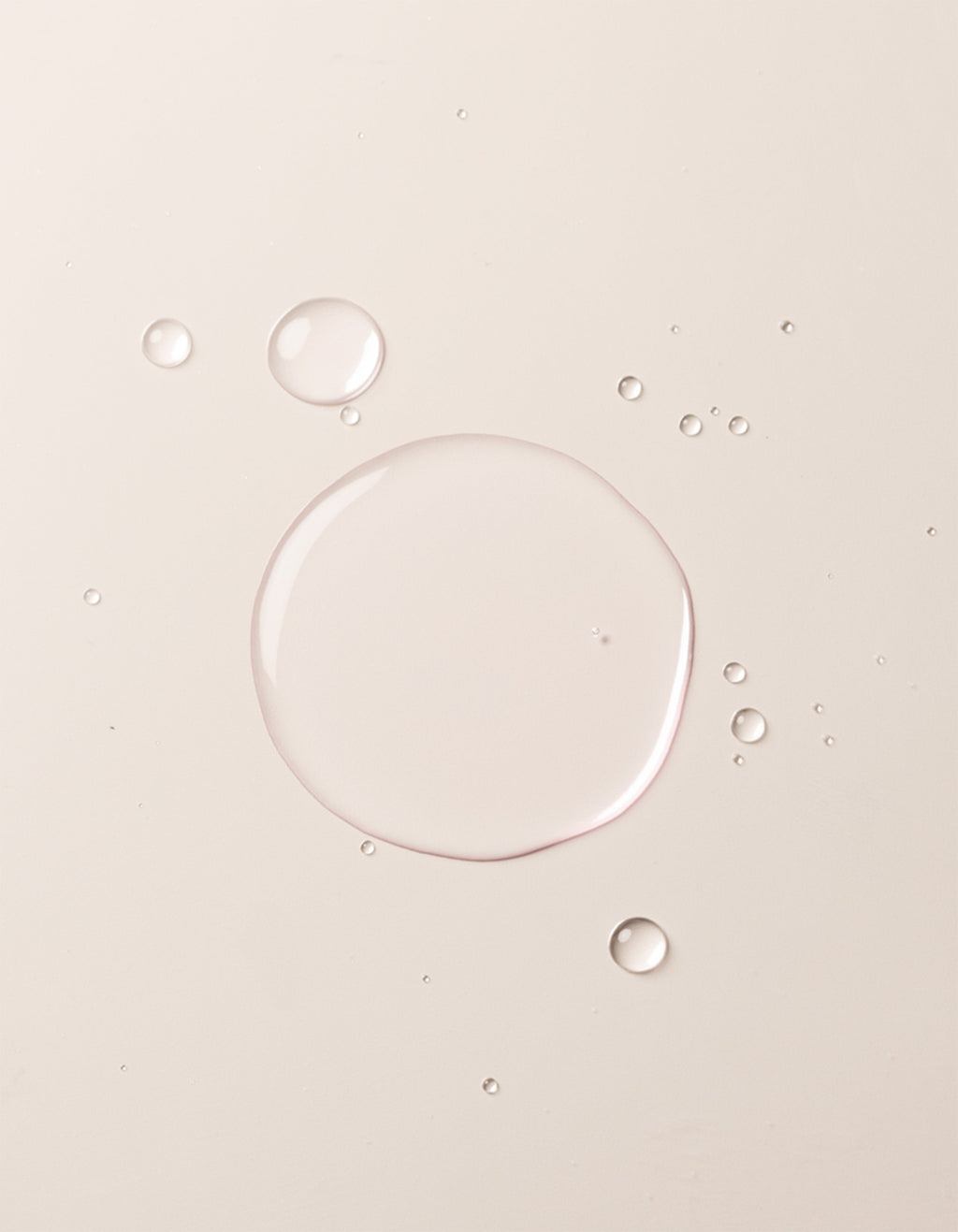 A close-up image showcases translucent liquid droplets of Cozy Earth's Balancing Face Mist on a smooth, off-white surface. The droplets vary in size, with one large central droplet surrounded by several smaller ones, creating a clean and minimalistic appearance. |Size:Full Size
