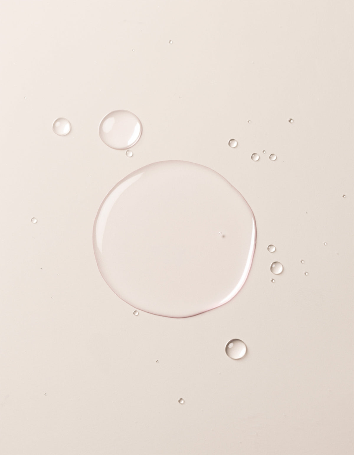 A close-up image showcases translucent liquid droplets of Cozy Earth's Balancing Face Mist on a smooth, off-white surface. The droplets vary in size, with one large central droplet surrounded by several smaller ones, creating a clean and minimalistic appearance. |Size:Full Size