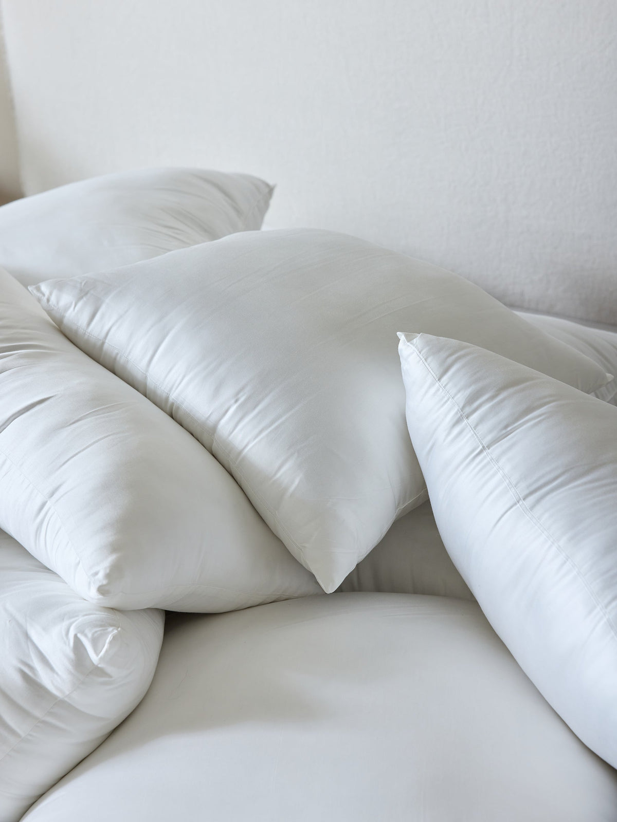A collection of Cozy Earth Premium Down Alternative Inserts stacked in various orientations. These inserts appear smooth and soft, with a plain white background enhancing their clean and fresh look. |Size:14" x 30"