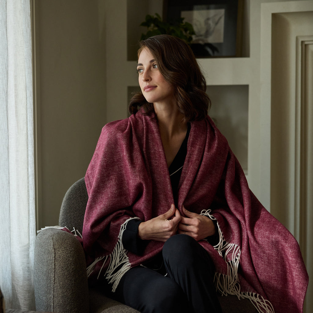 Woman sitting down with berry herringbone tassel throw wrapped around her |Color:Berry