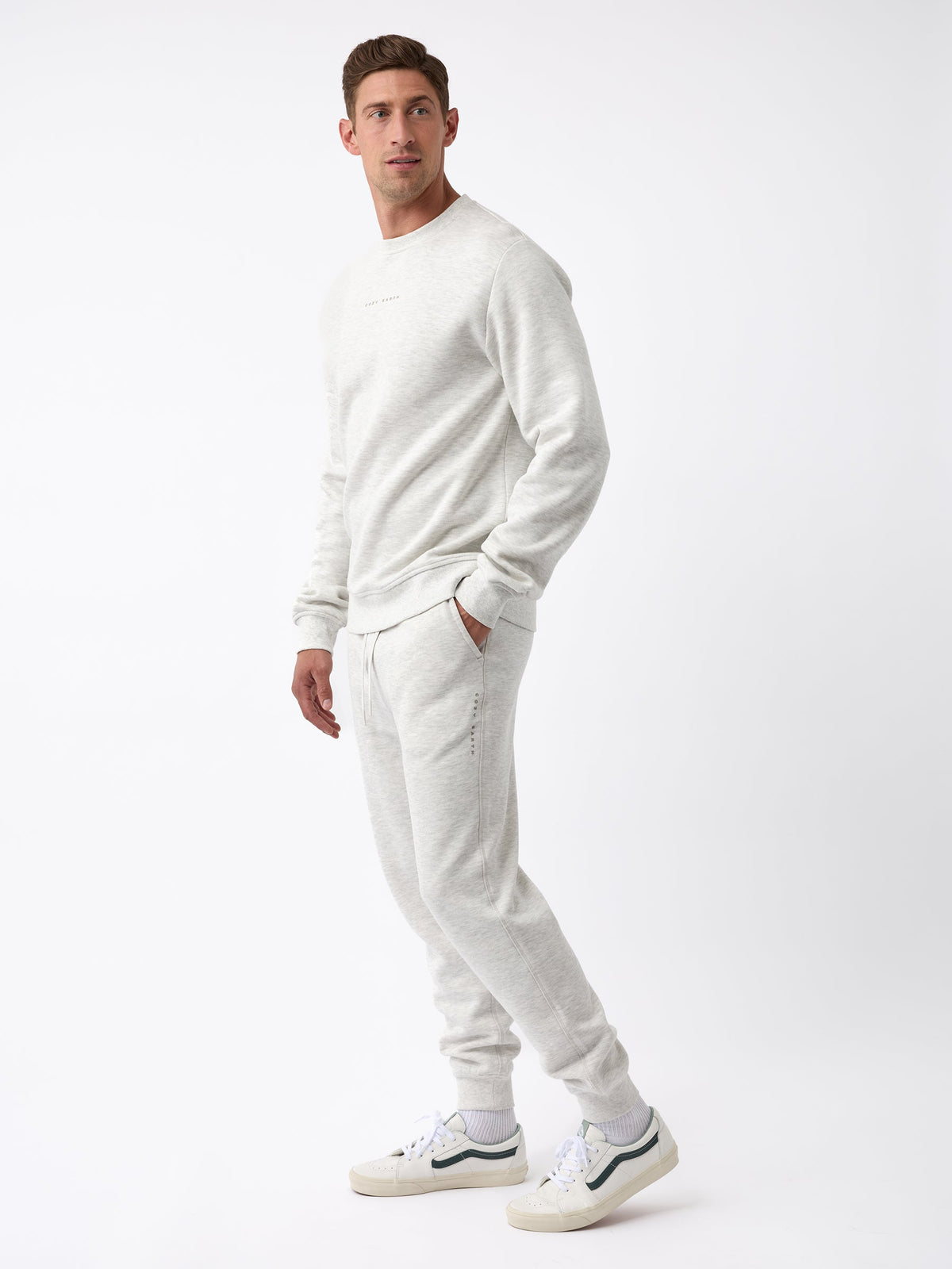 A person stands against a white background, dressed in the Men's CityScape Jogger by Cozy Earth, paired with white sneakers. The outfit exudes a casual and comfortable vibe. |Color:Heather Grey