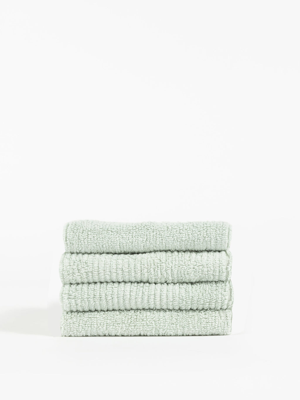 A stack of four neatly folded, Cozy Earth Ribbed Terry Washcloths in light green is placed against a plain white background. The texture of these washcloths appears soft and plush, with visible ribbed detailing in the fabric. The overall look is clean and minimalistic. |Color:Laurel