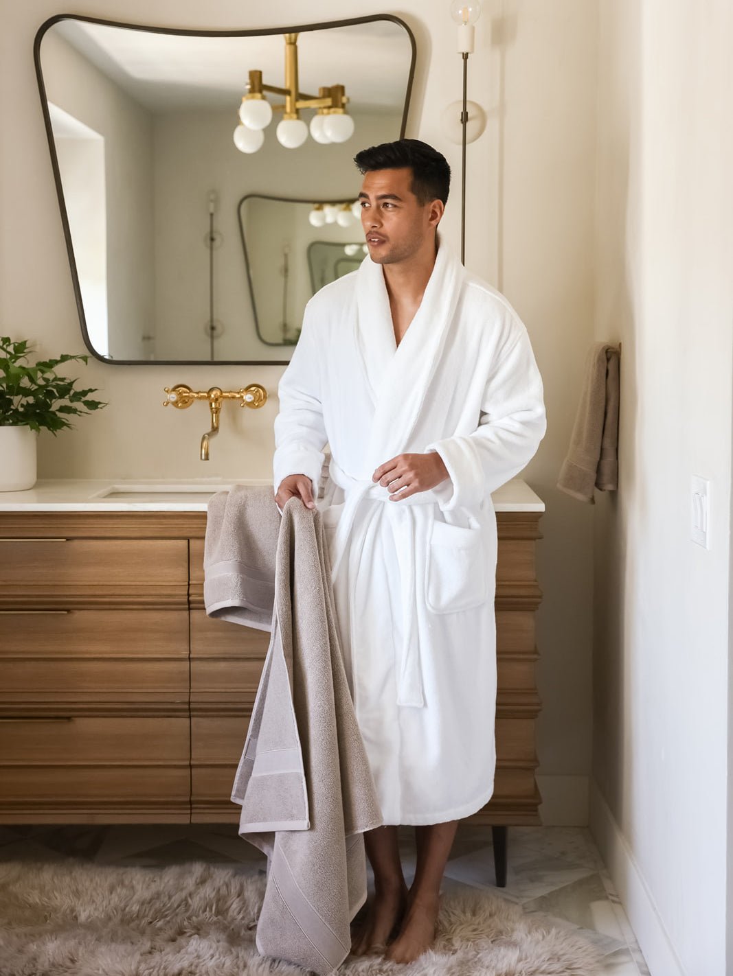 Man in white robe standing in bathroom with sand luxe bath sheet |Color:Sand