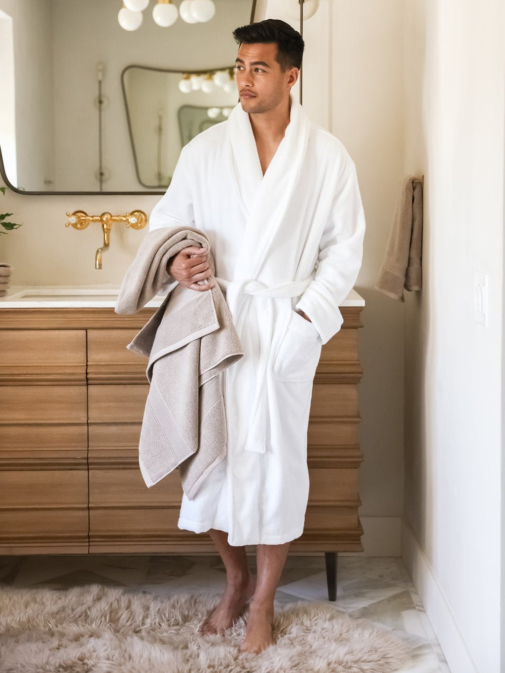 Man in white robe holding sand luxe bath sheet |Color:Sand