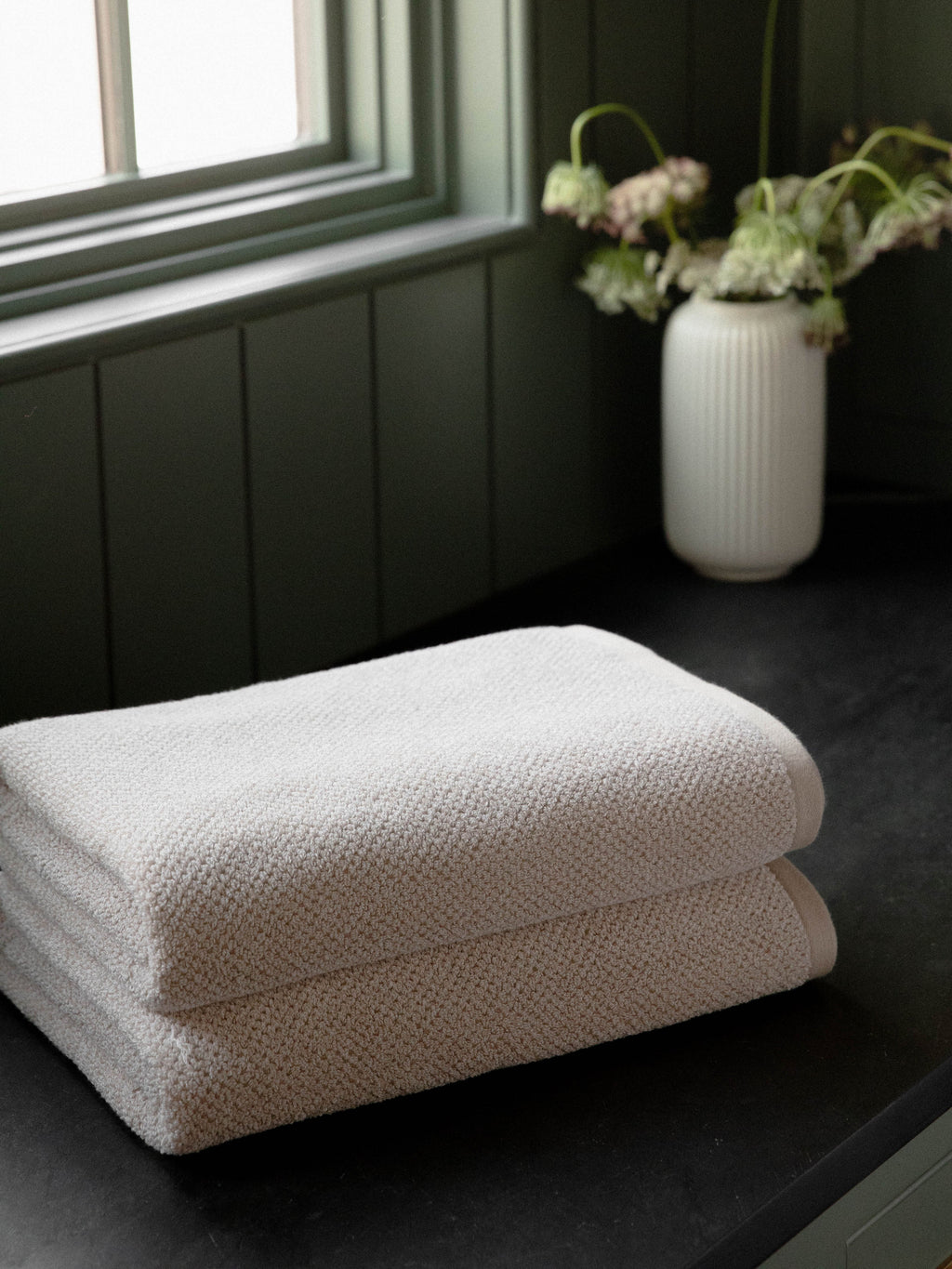 Nantucket Bath Towels in the color Heathered Sand. Photo of Nantucket Bath Towels taken with the bath towels resting on a countertop in a bathroom. |Color:Heathered Sand