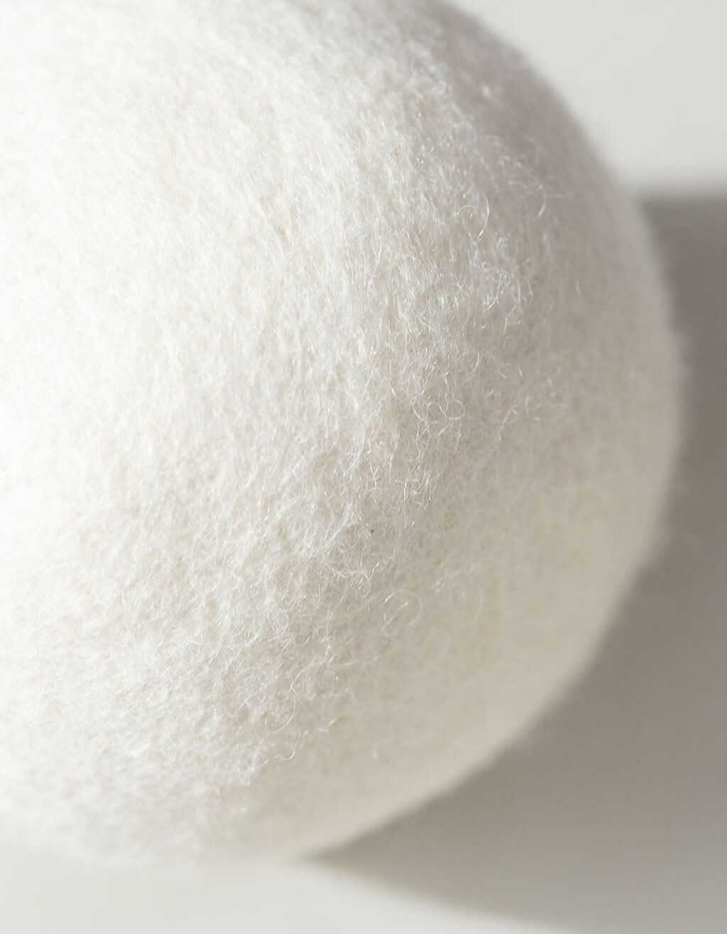 Close-up of a white, textured Wool Dryer Ball by Cozy Earth, made of felted wool, with soft lighting and a gentle shadow on a light surface.|Size:Regular