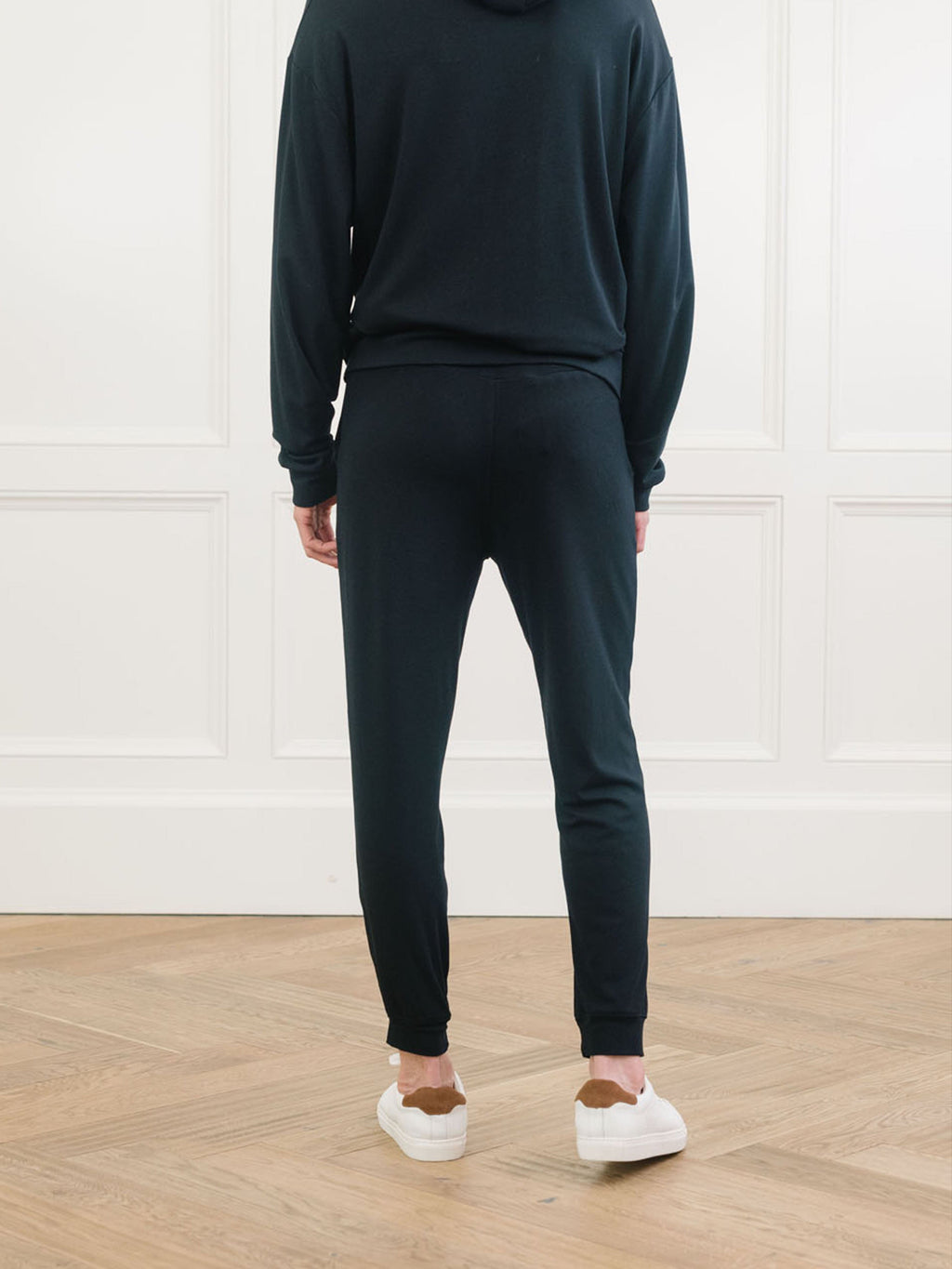 A man pictured from the waist down wears Men's Brushed Bamboo Hoodie & Jogger Set in Black. He faces away from the camera. |Color:Black