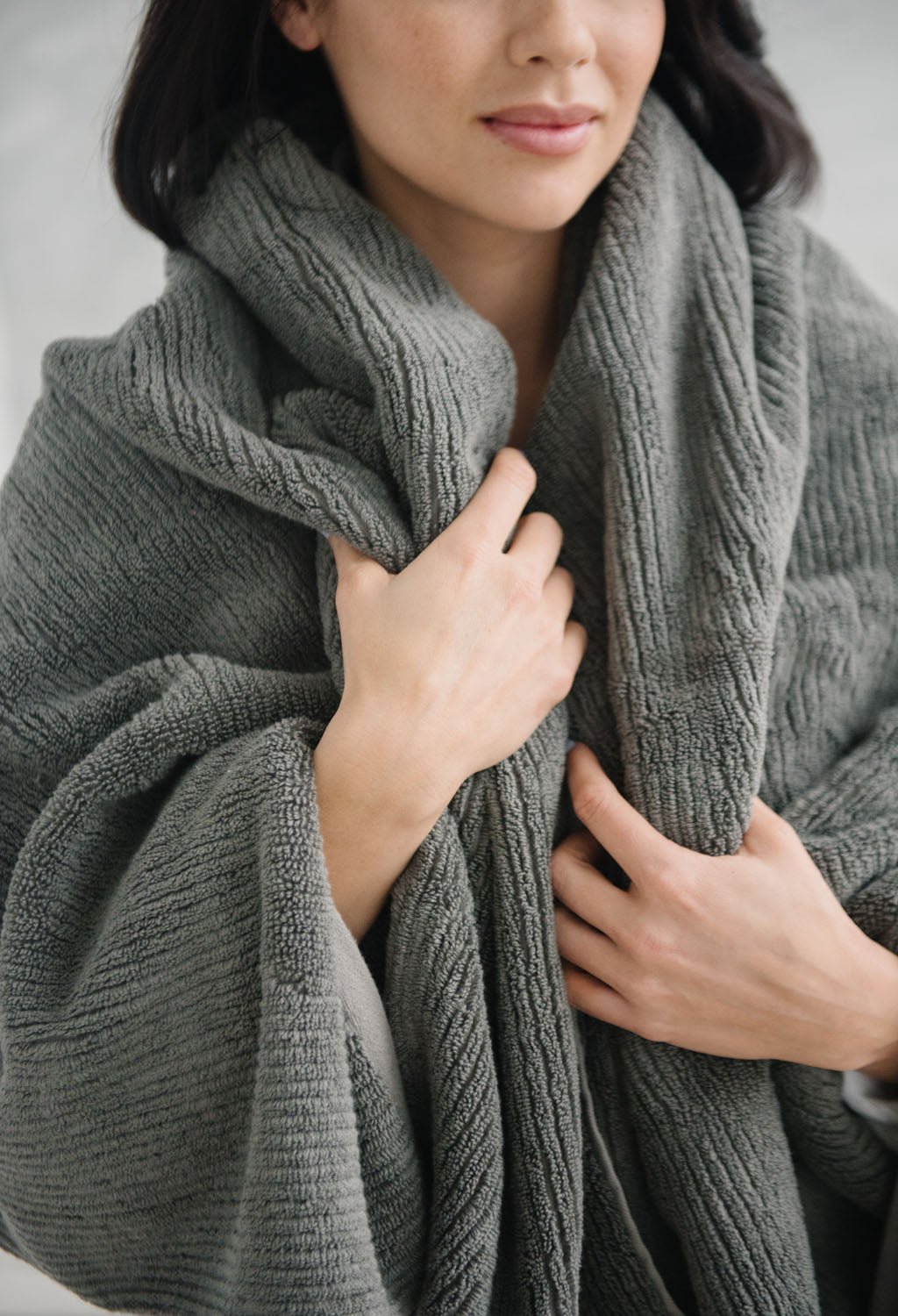 Ribbed Terry Bath Sheets in the color Charcoal. Photo of product taken in a bathroom as a woman wears the towel. |Color:Charcoal