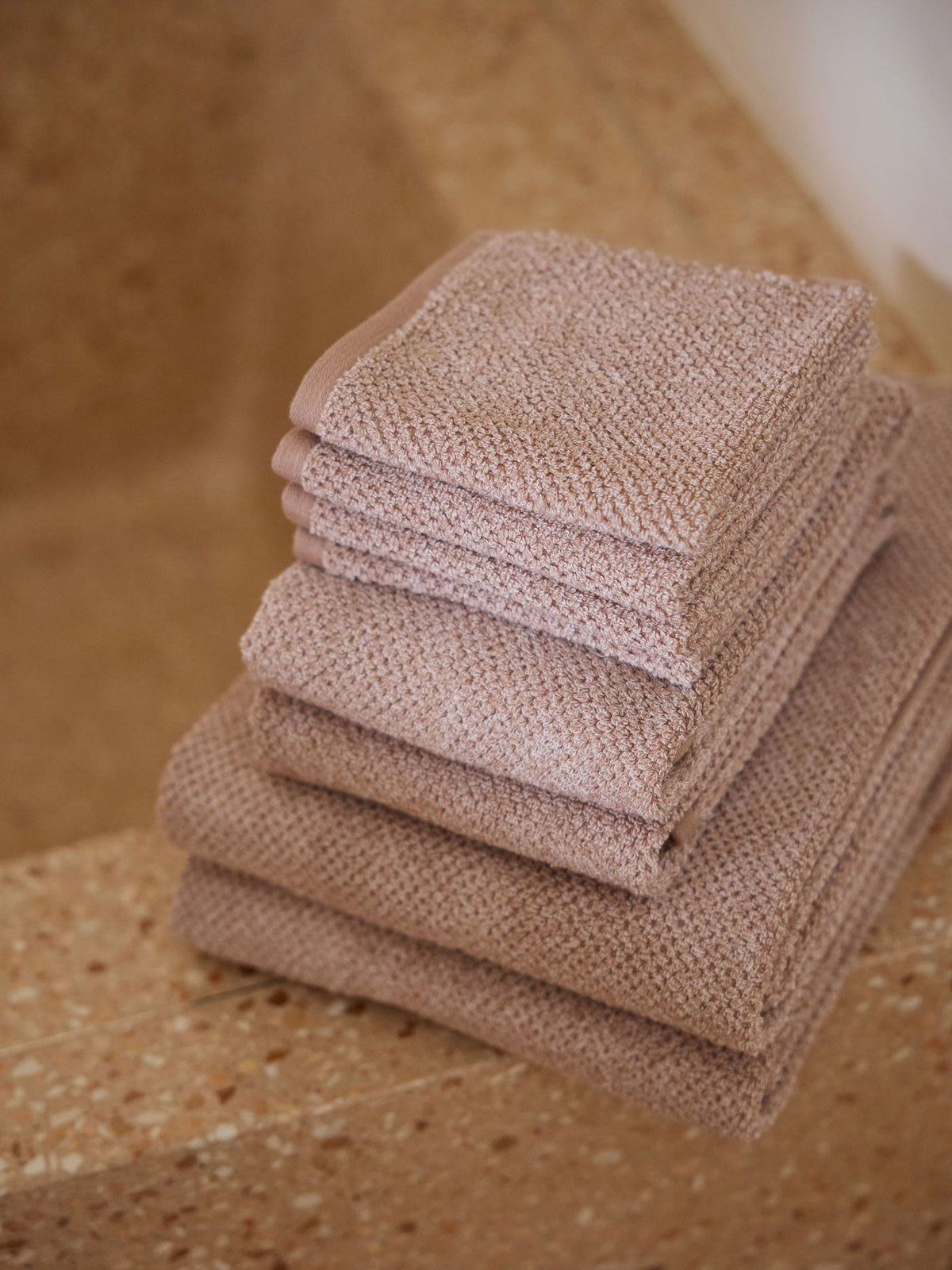 A stack of Cozy Earth bath towels sit on the edge of a stone bathtub. |Color:Heathered Clay