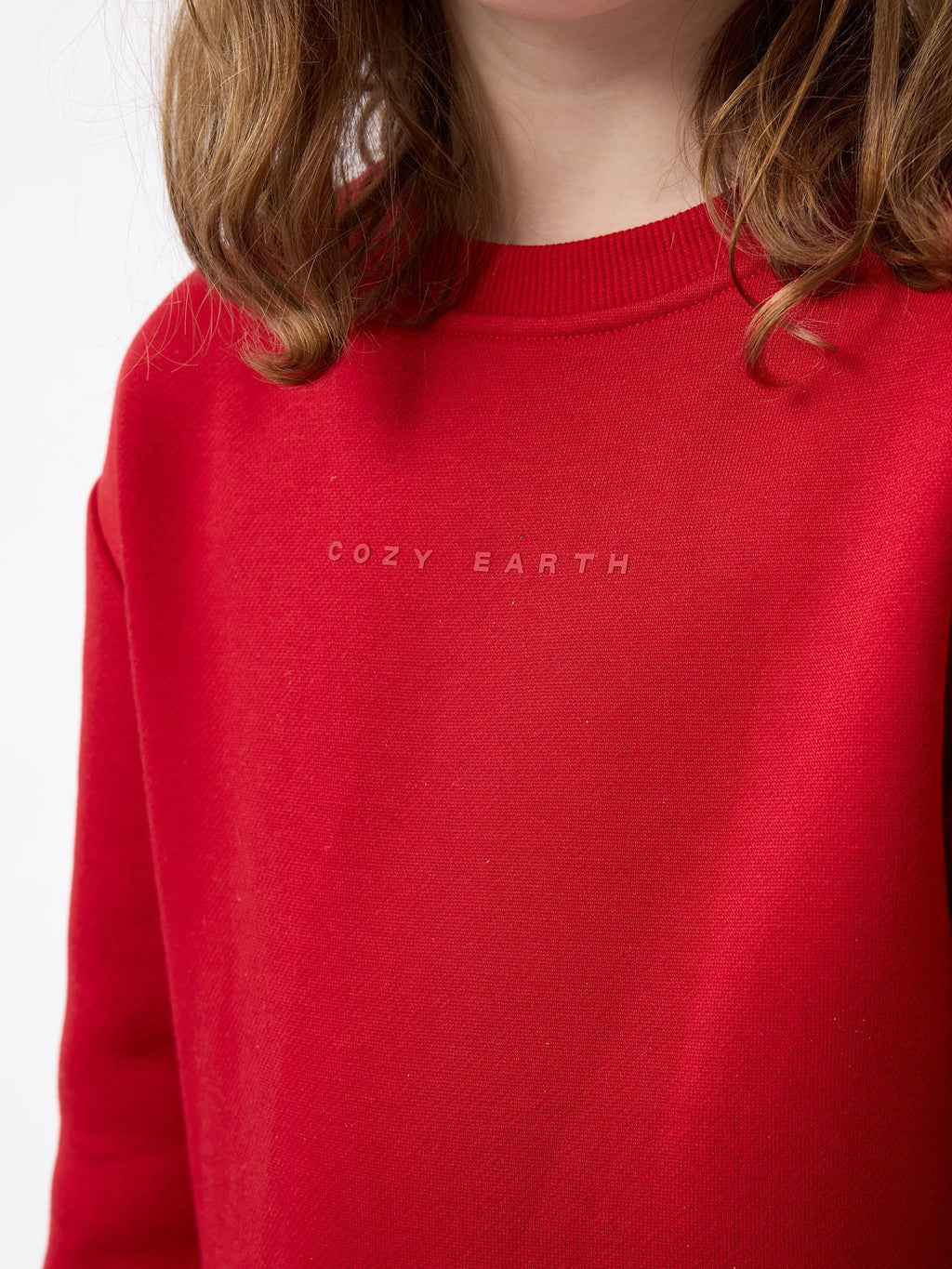 A person with shoulder-length hair wearing a red Kid's CityScape Crewneck by Cozy Earth. The background is plain white. |Color:Crimson