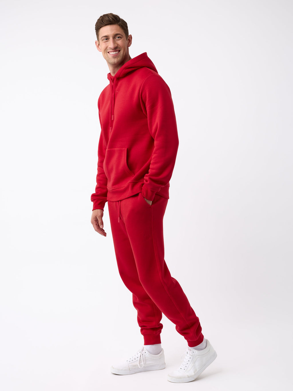 A person stands smiling, dressed in a matching Cozy Earth red hoodie and Men's CityScape Jogger, complemented by white sneakers against a plain white background. |Color:Crimson
