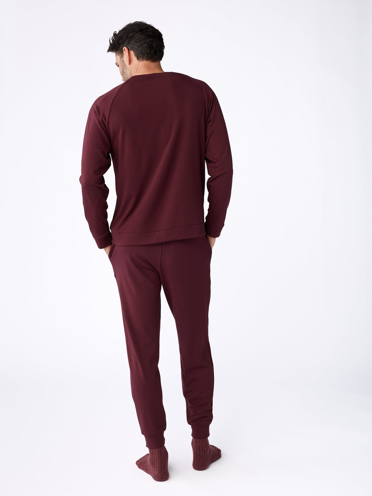 A person stands facing away, wearing the Men's Ultra-Soft Bamboo Pullover Crew from Cozy Earth in maroon, paired with matching pants. They are barefoot, set against a plain white background. |Color:Burgundy