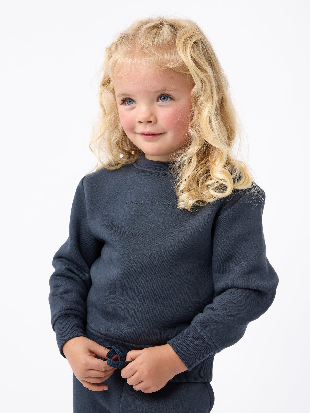 A young child with curly blonde hair is wearing Cozy Earth's Kid's CityScape Crewneck and looking slightly to the side against a plain white background. |Color:Eclipse