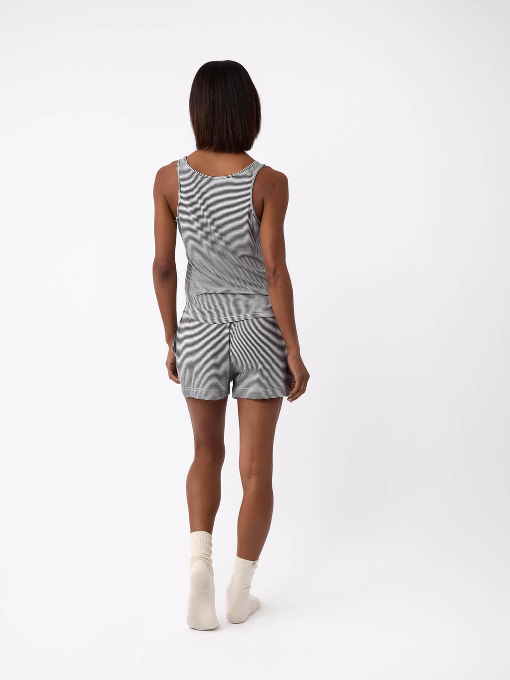 A person stands with their back to the camera, wearing a Cozy Earth Women's Bamboo Stretch-Knit Lounge Tank in gray, paired with matching shorts and white socks, set against a plain white background. |Color:Eclipse Mini Stripe