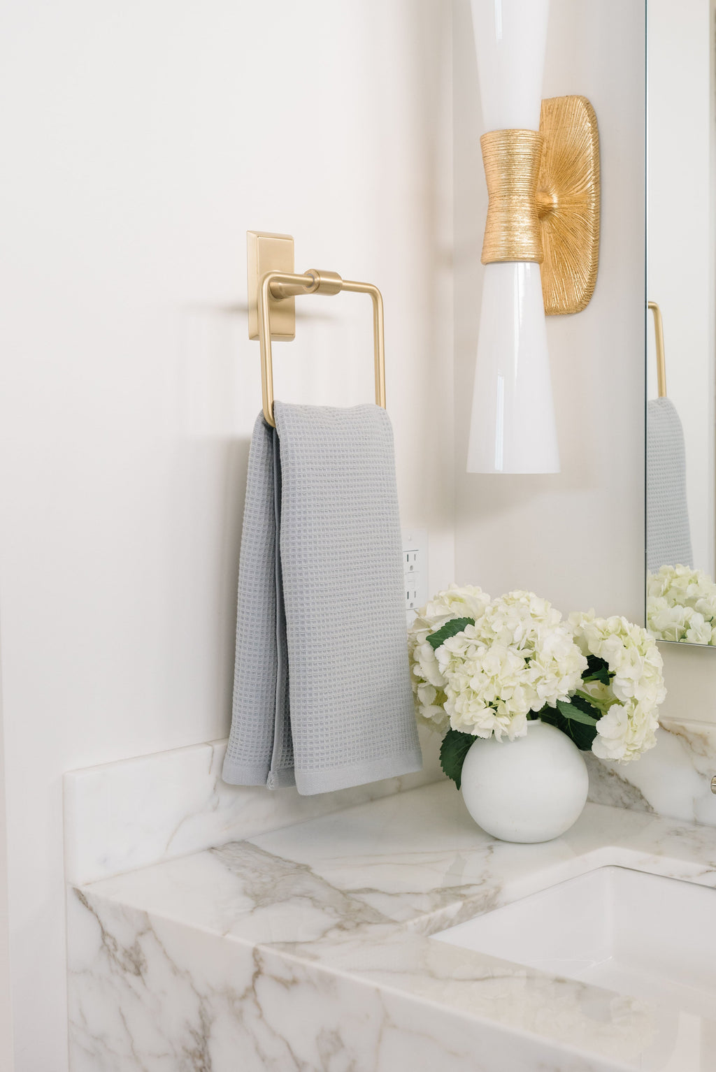 Harbor Mist Waffle Hand Towel hanging from a gold towel ring. The photo was taken at a white marble bathroom sink. |Color:Harbor Mist