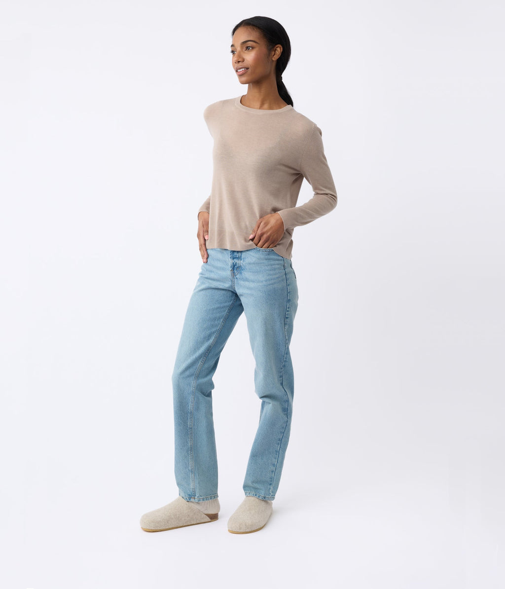 A person wearing a beige sweater, light blue jeans, and Cozy Earth's Lakehouse Clog stands against a plain white background, smiling with hands on hips. |Color:Oat