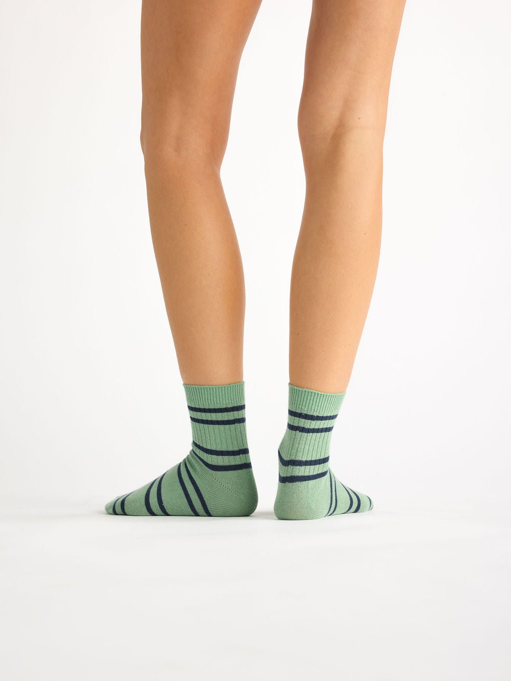 A person faces away from the camera, showcasing Cozy Earth's Women's Sadie Sock in green with dark blue horizontal stripes against a plain white background. |Color:Wintergreen/Eclipse