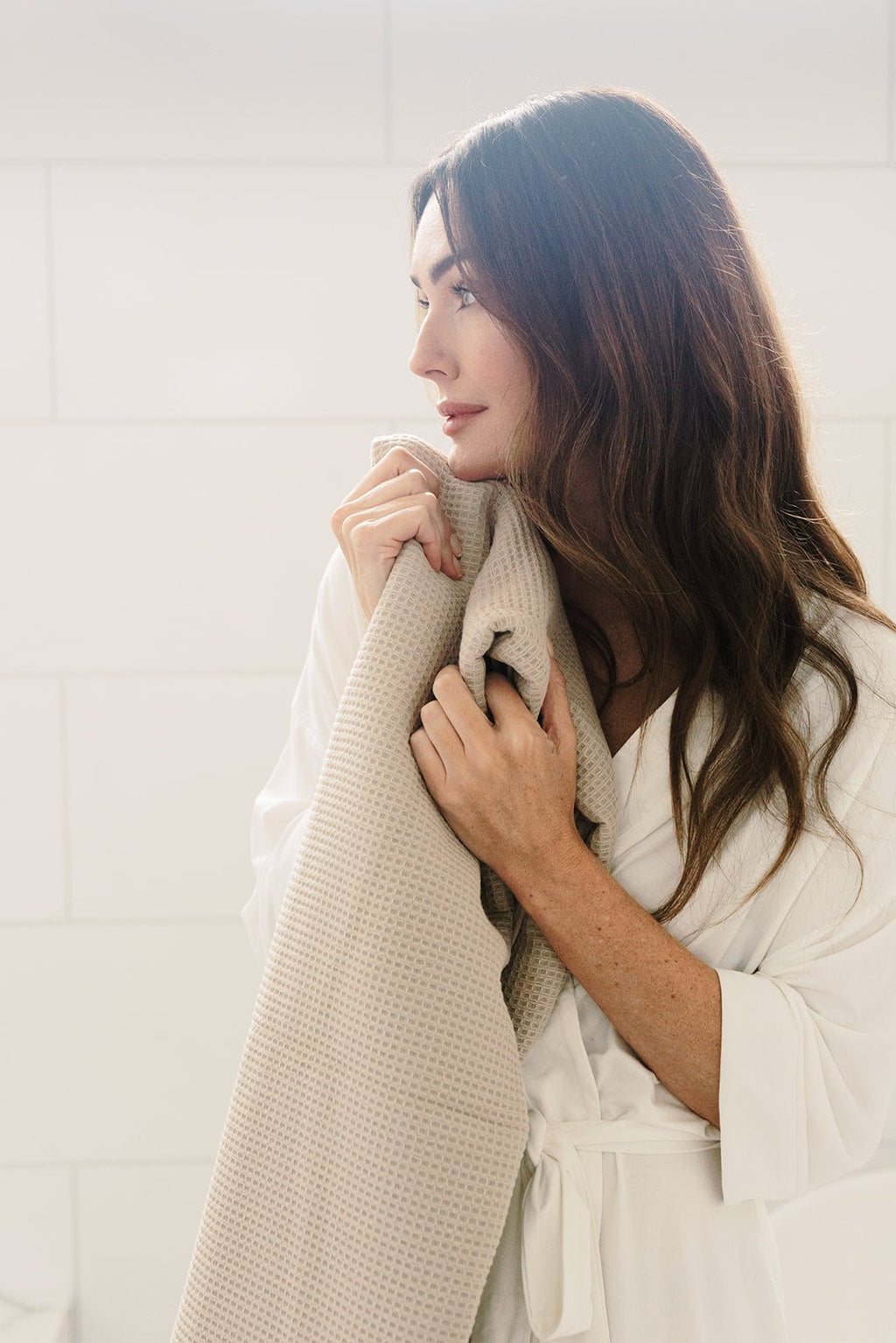 Waffle Bath Towel in the color Sand. Photo of Sand Waffle Bath Towel taken with a brunette woman holding the Sand Waffle Bath Towel close to her body |Color:Sand
