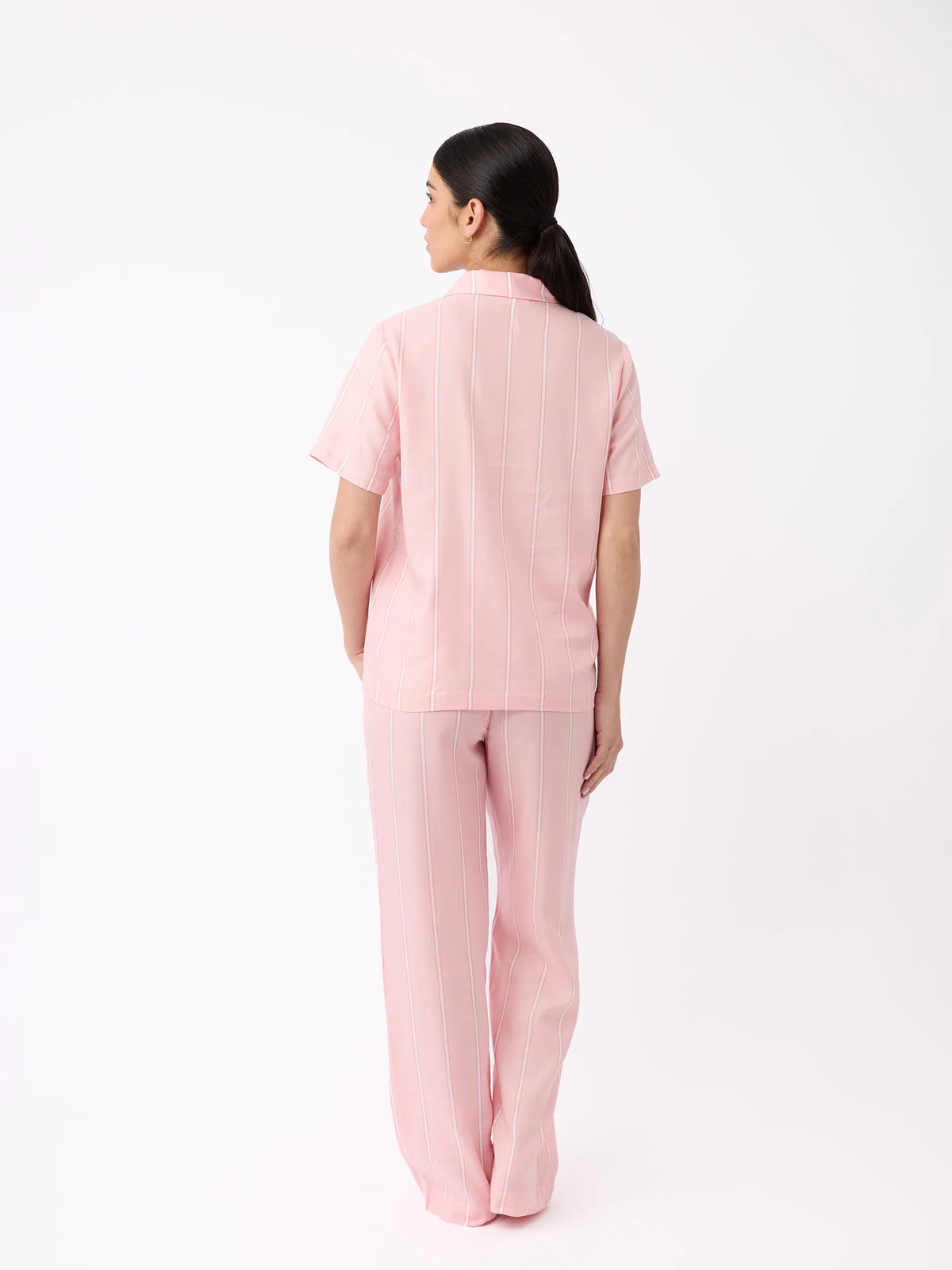 A woman with long dark hair, back to the camera, wears Cozy Earth's pink short-sleeve top and Women's Soft Woven Pajama Pant with subtle vertical stripes against a plain white background. |Color:Sweetheart Stripe