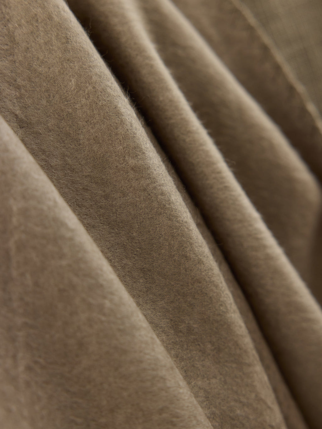 A close-up image of the Bamboo Tassel Throw by Cozy Earth reveals its beige, soft, fuzzy texture. The throw appears to be folded, displaying gentle, flowing creases and shadows. |Color:Walnut