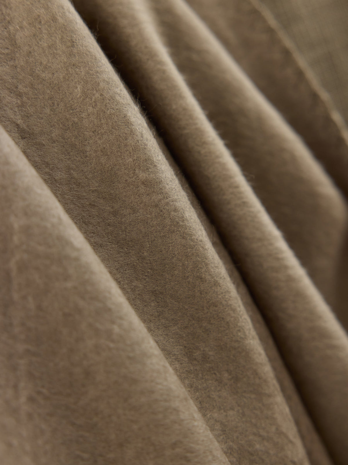 A close-up image of the Bamboo Tassel Throw by Cozy Earth reveals its beige, soft, fuzzy texture. The throw appears to be folded, displaying gentle, flowing creases and shadows. |Color:Walnut