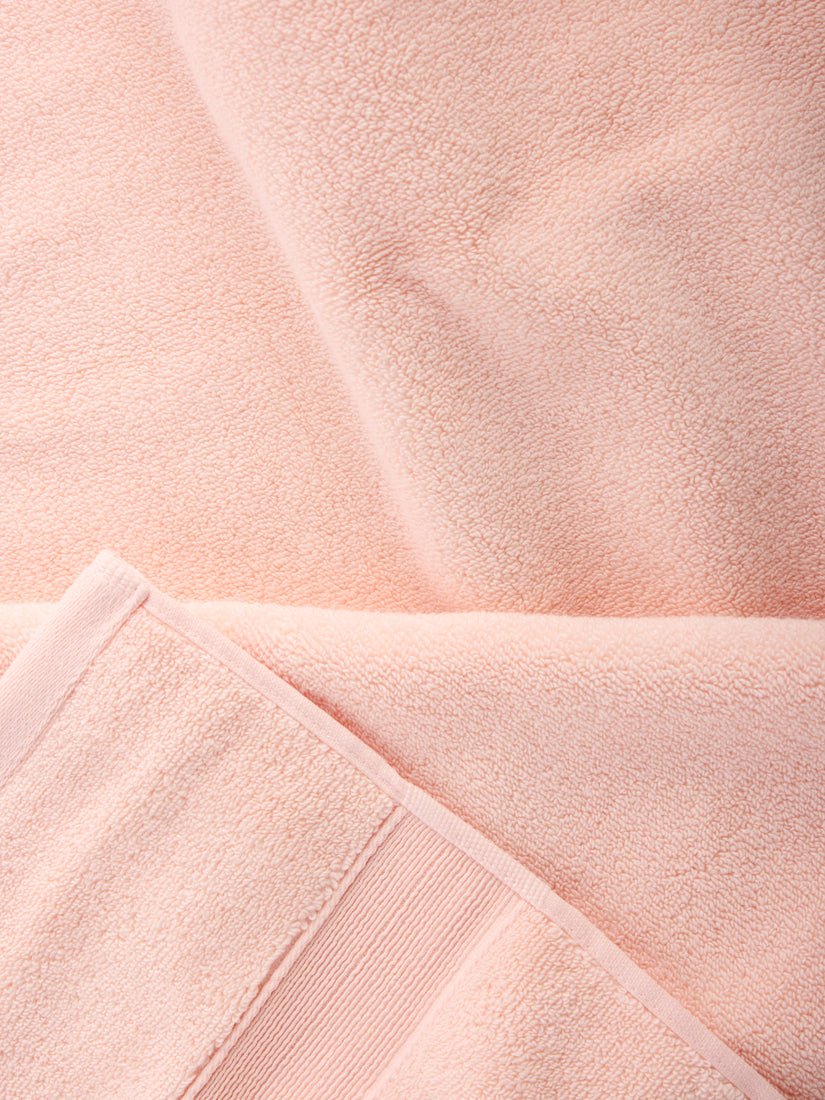 A close-up of the Luxe Bath Towel Set from Cozy Earth showcases their soft, peach-colored texture. The towels are folded neatly, with visible stitching along the edges and a subtle, plush surface. |Color:Blossom
