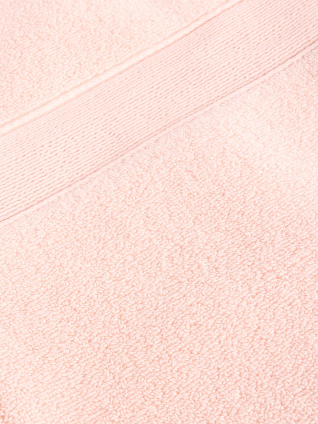 A close-up of a Luxe Washcloth by Cozy Earth reveals the textured fabric in soft, pastel pink, featuring a smooth horizontal band with a fine line pattern running across it. |Color:Blossom