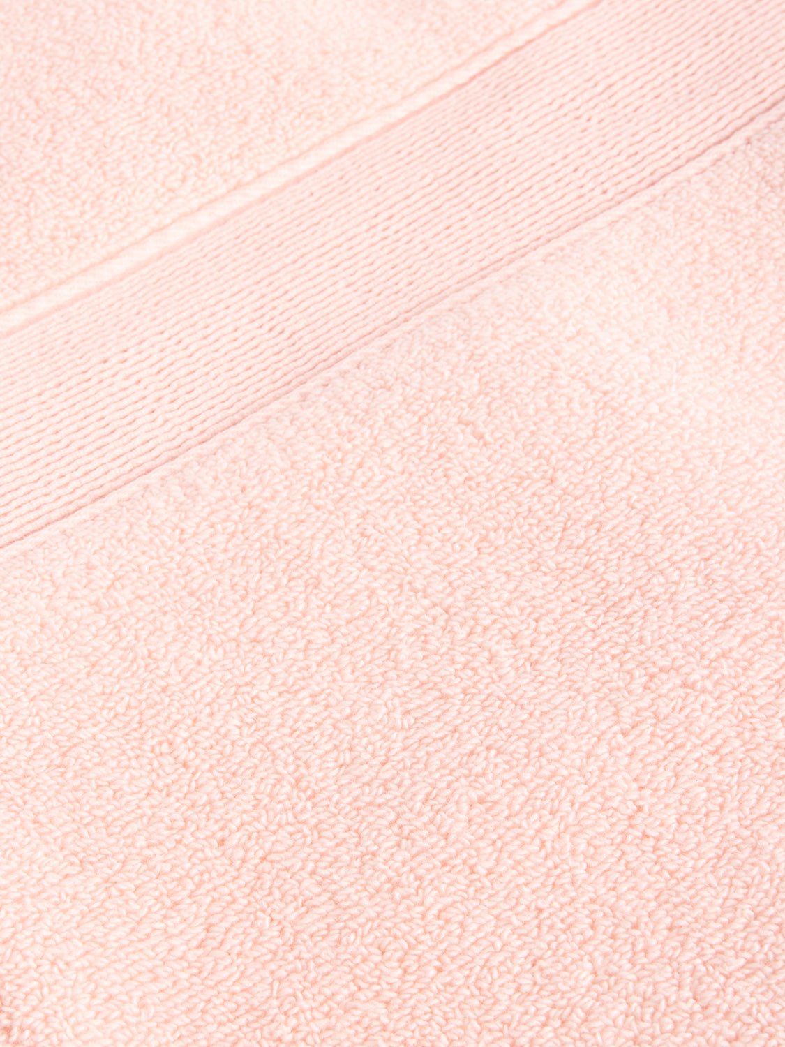A close-up of a Luxe Washcloth by Cozy Earth reveals the textured fabric in soft, pastel pink, featuring a smooth horizontal band with a fine line pattern running across it. |Color:Blossom